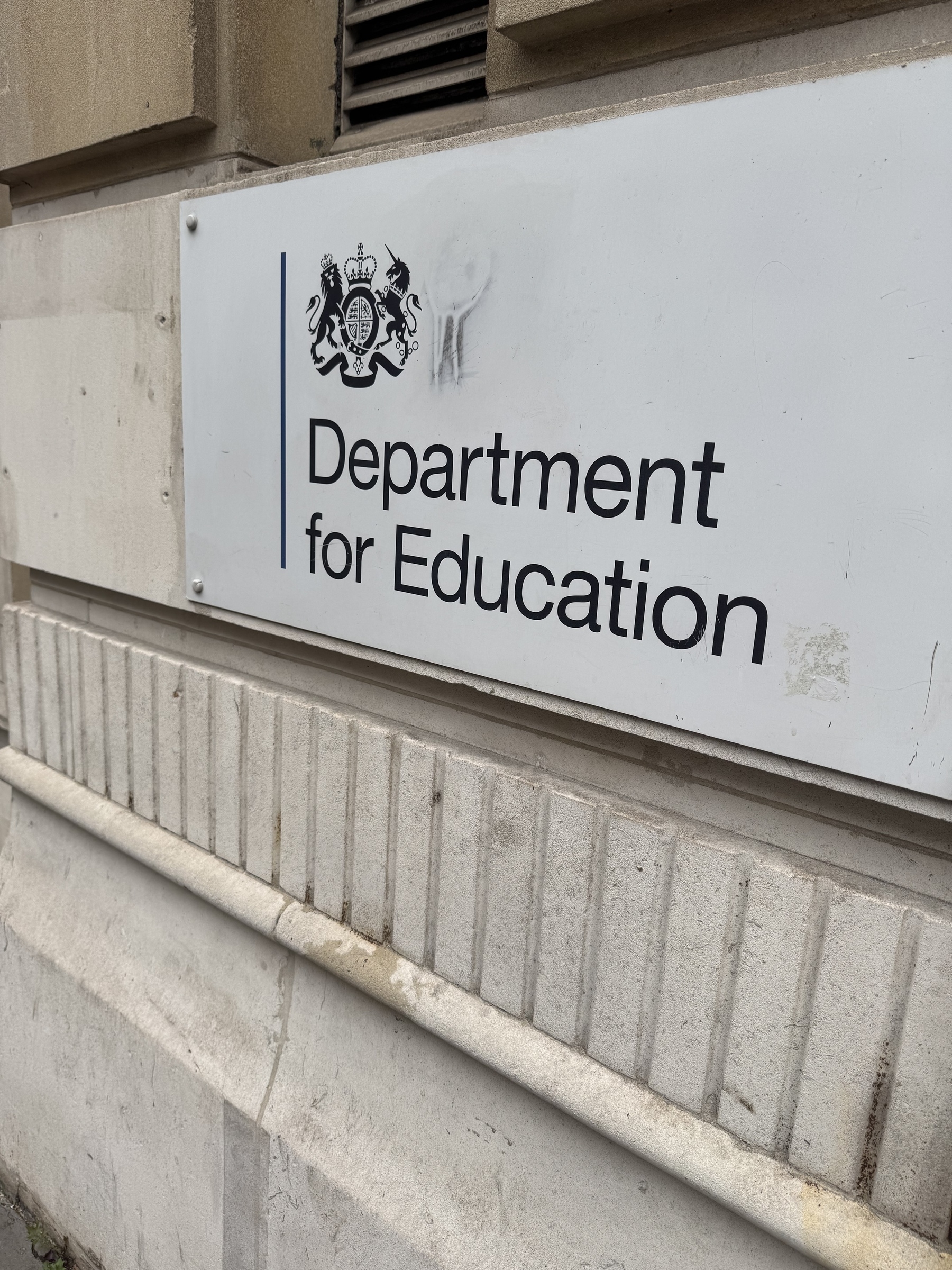 A sign for the Department for Education is mounted on a stone wall.