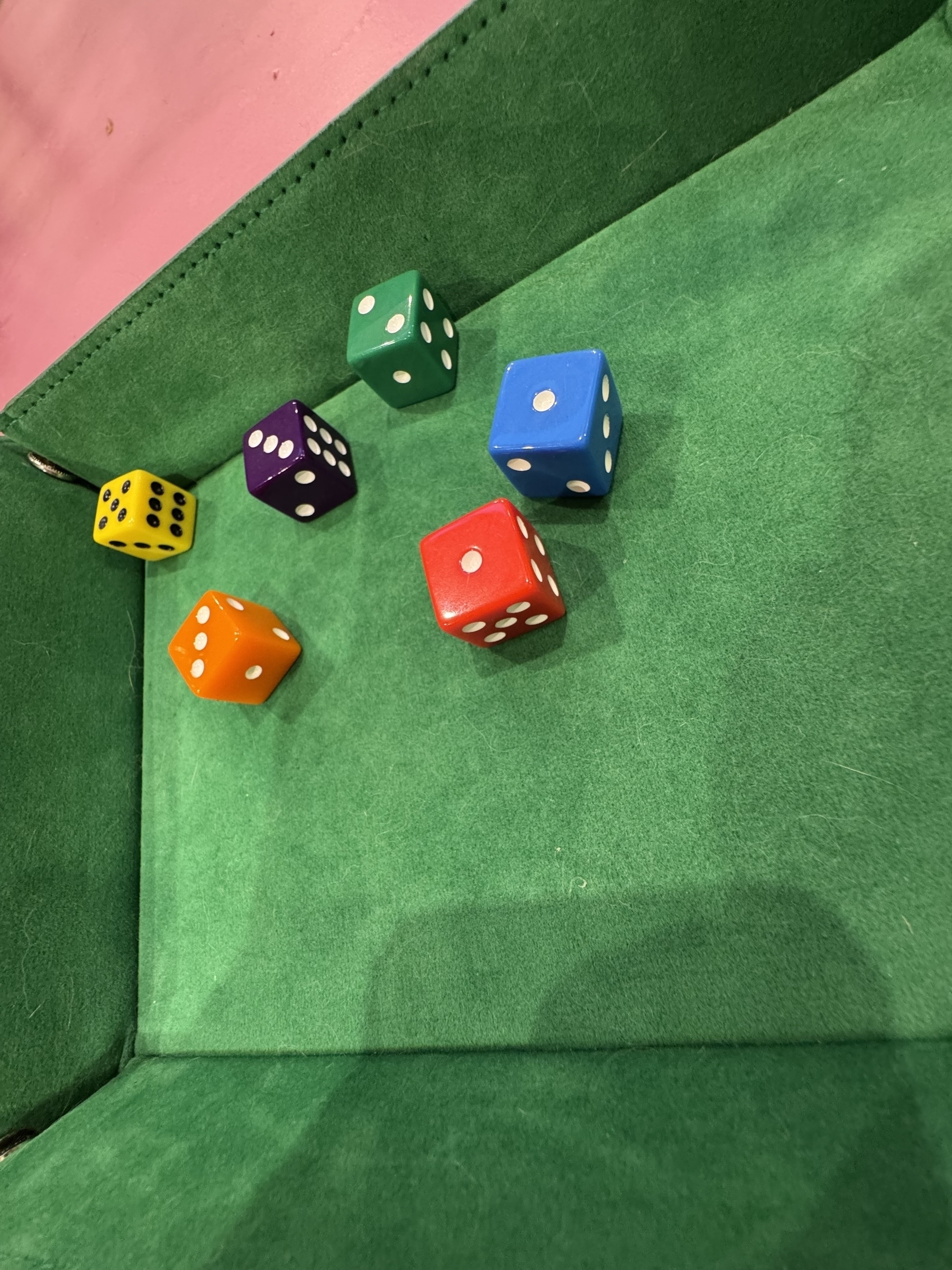 Five colorful dice are scattered inside a green felt tray.
