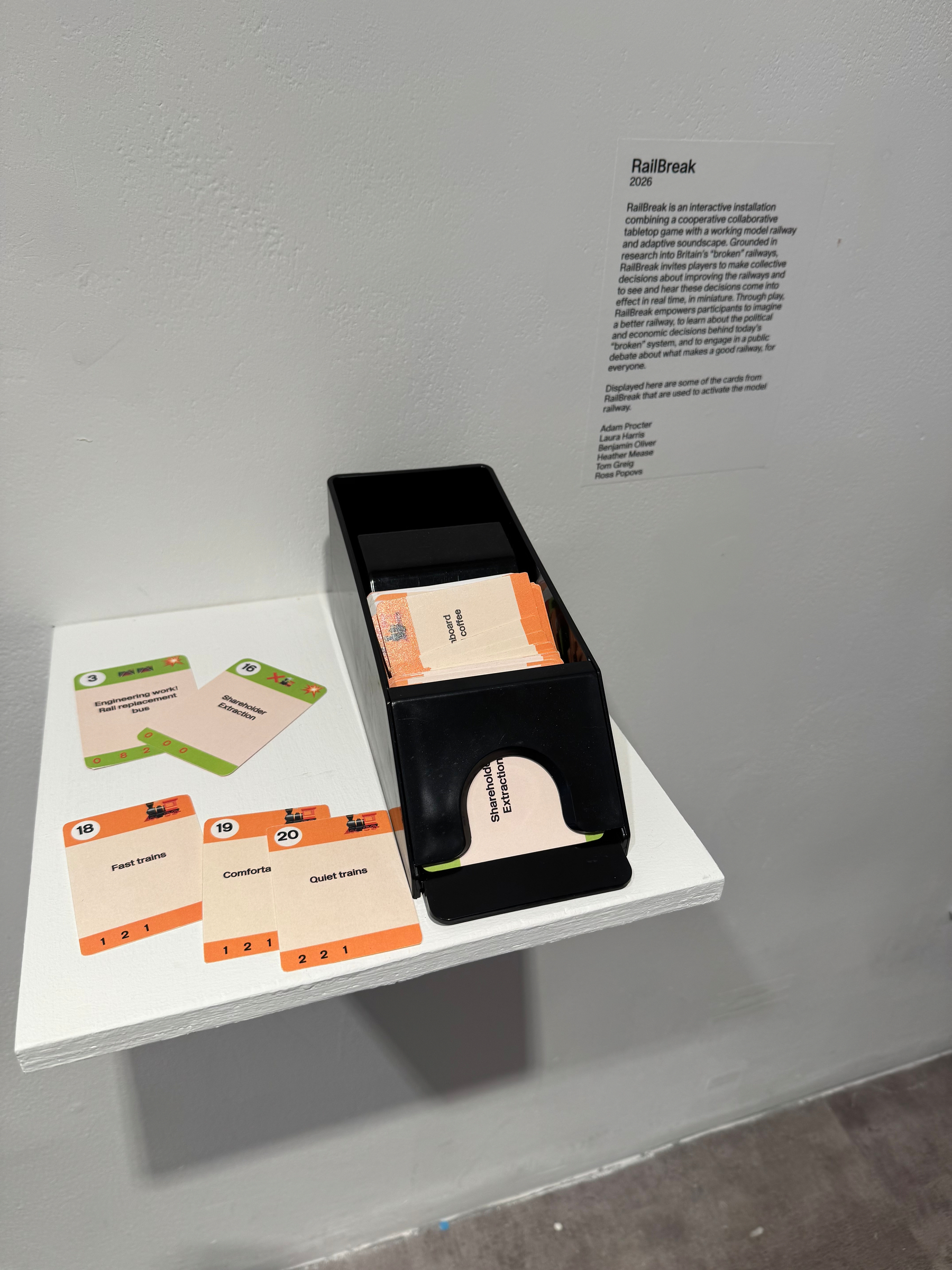 A black card dispenser and several cards are placed on a small white shelf next to a wall with explanatory text about RailBreak.
