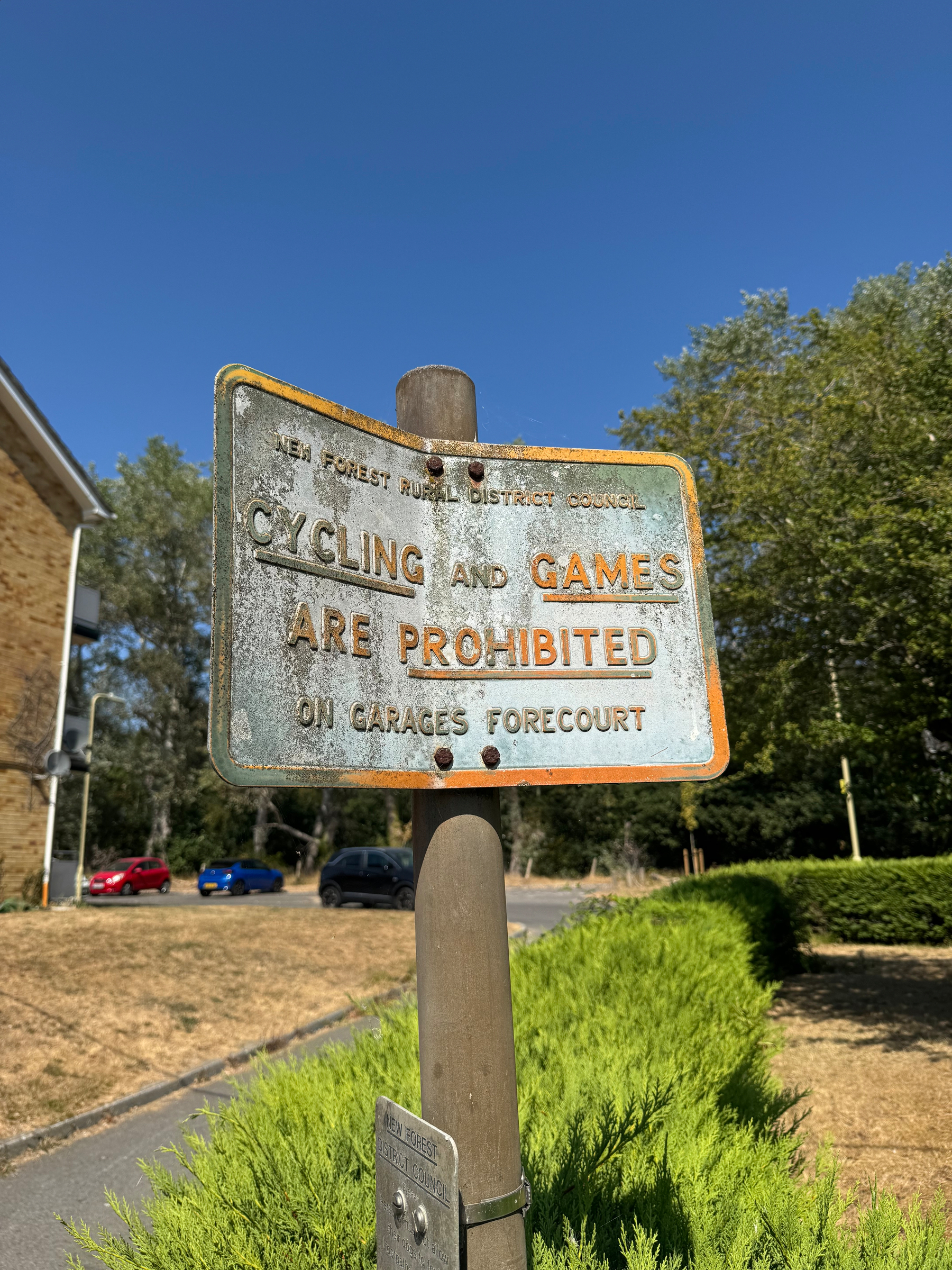 A weathered metal sign on a pole warns that cycling and games are prohibited on the garages forecourt.