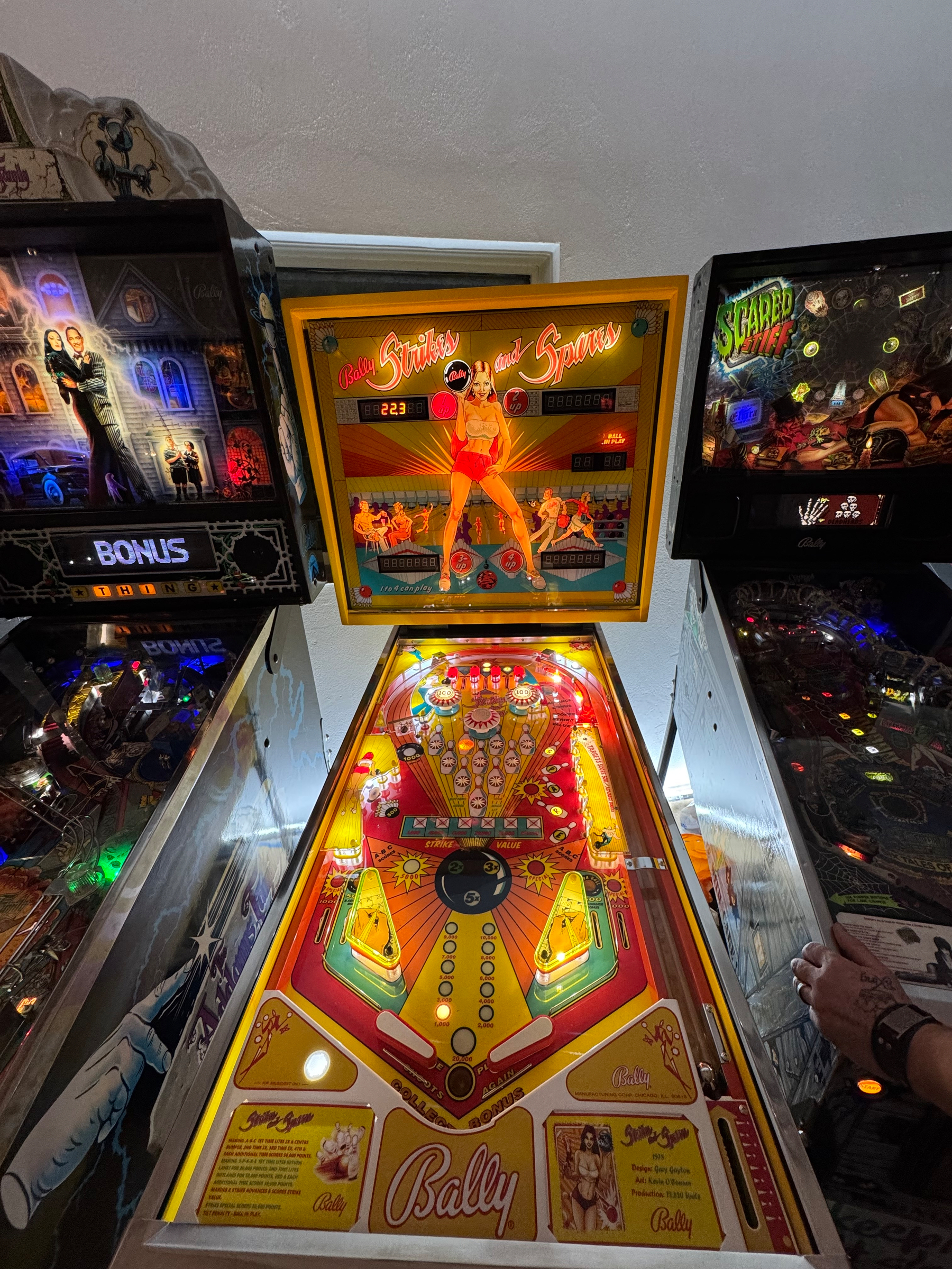A brightly illuminated vintage pinball machine is flanked by two darker-themed pinball machines in an arcade setting.