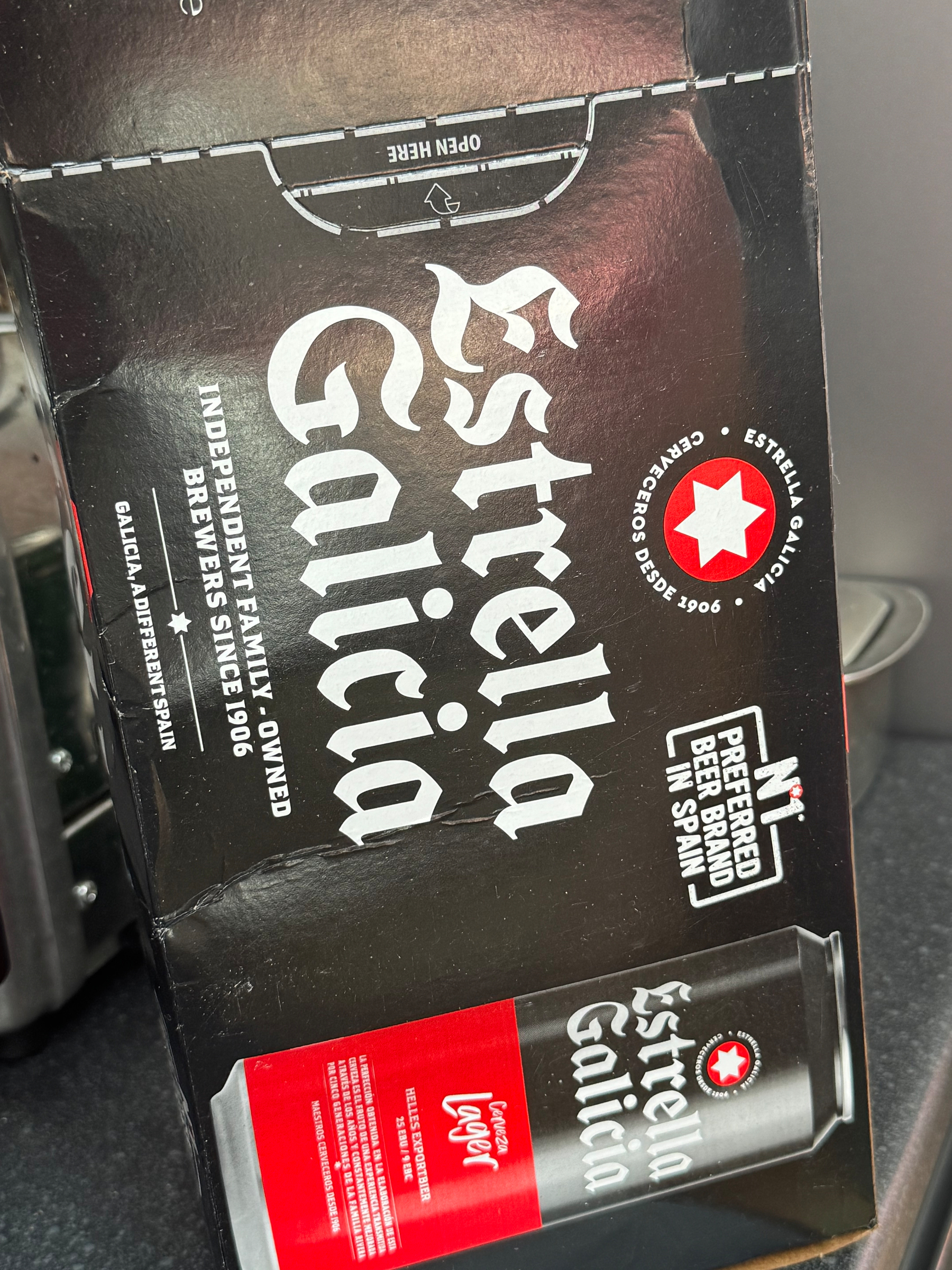 A package of Estrella Galicia beer featuring branding details such as being an independent family-owned brewery since 1906 and a preferred beer brand in Spain is shown.