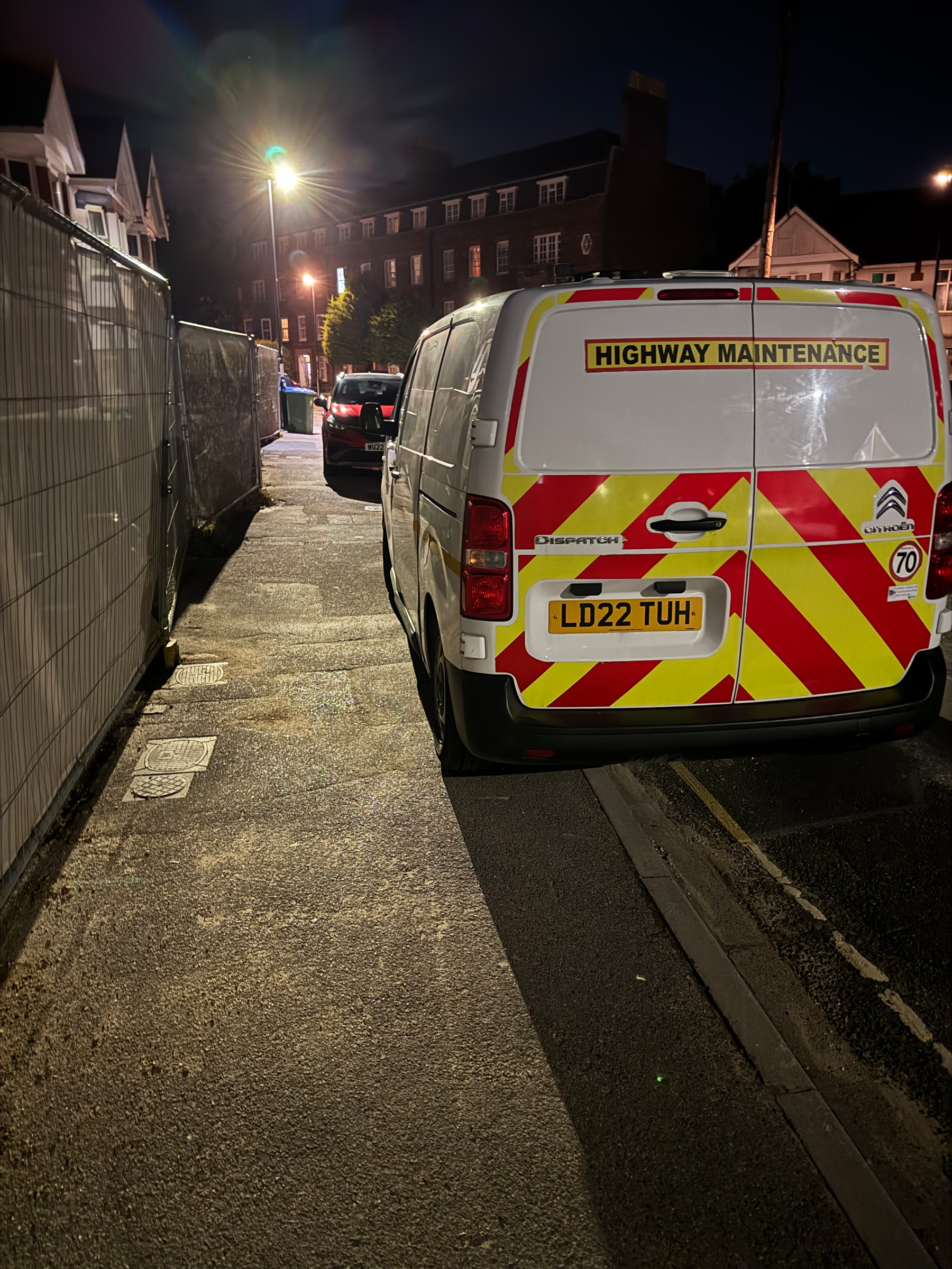 A white highway maintenance van with red and yellow chevron markings is parked on a dimly lit street at night.