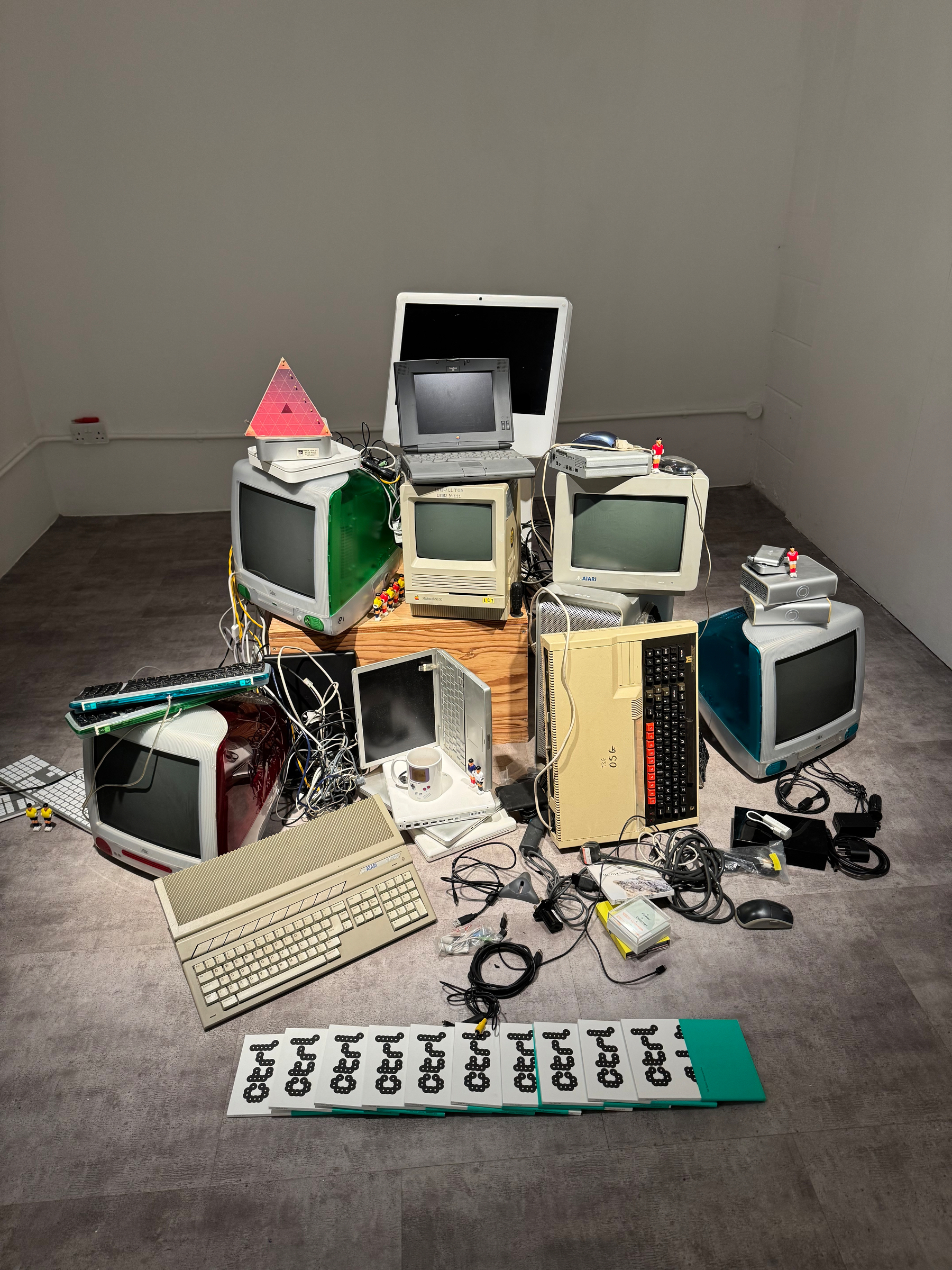 A collection of retro computers and monitors is arranged in a corner with tangled cables and devices.