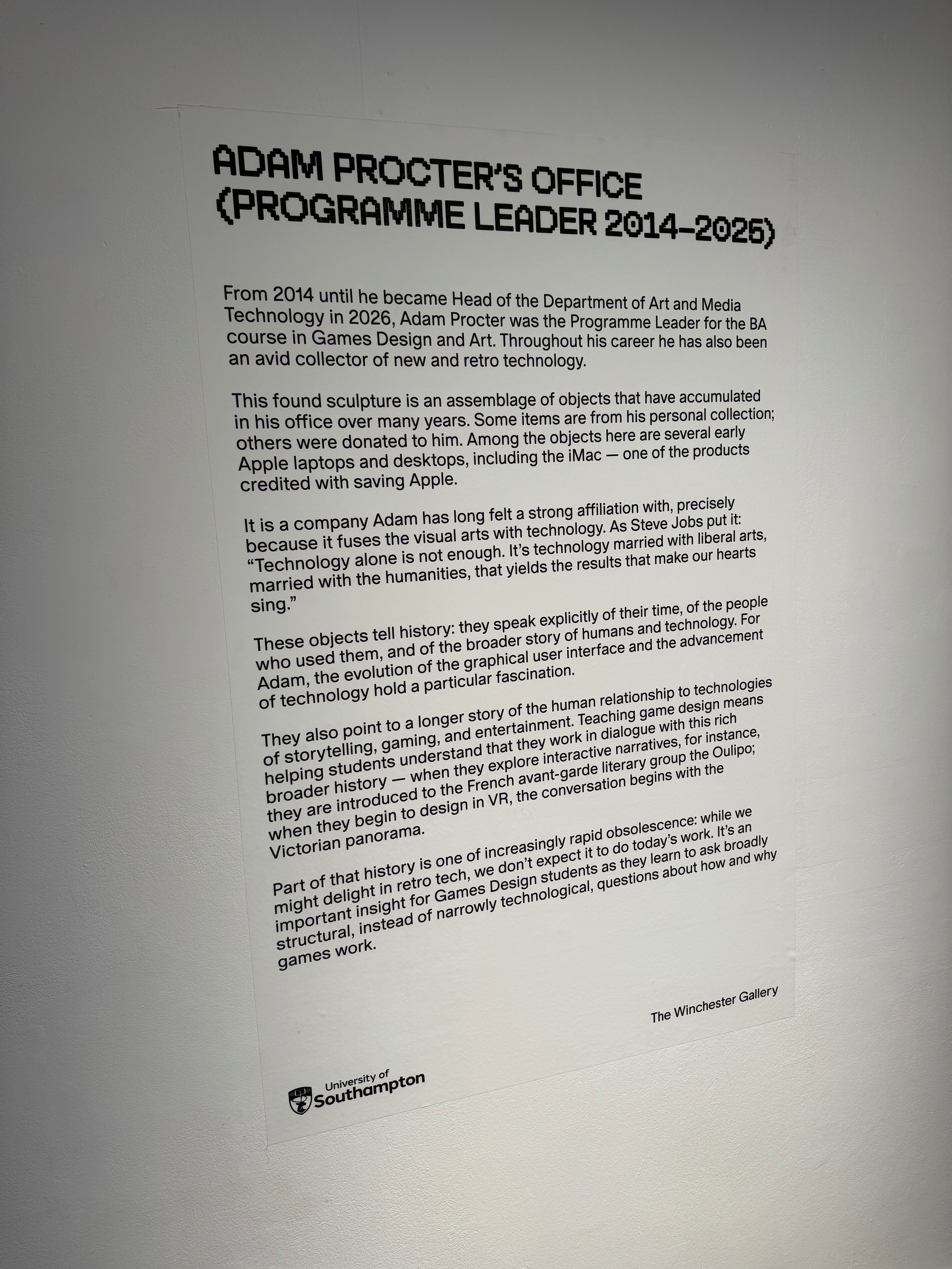 A wall display describes Adam Procter's role and collection of objects related to art and media, accompanied by details of an exhibition at The Winchester Gallery.