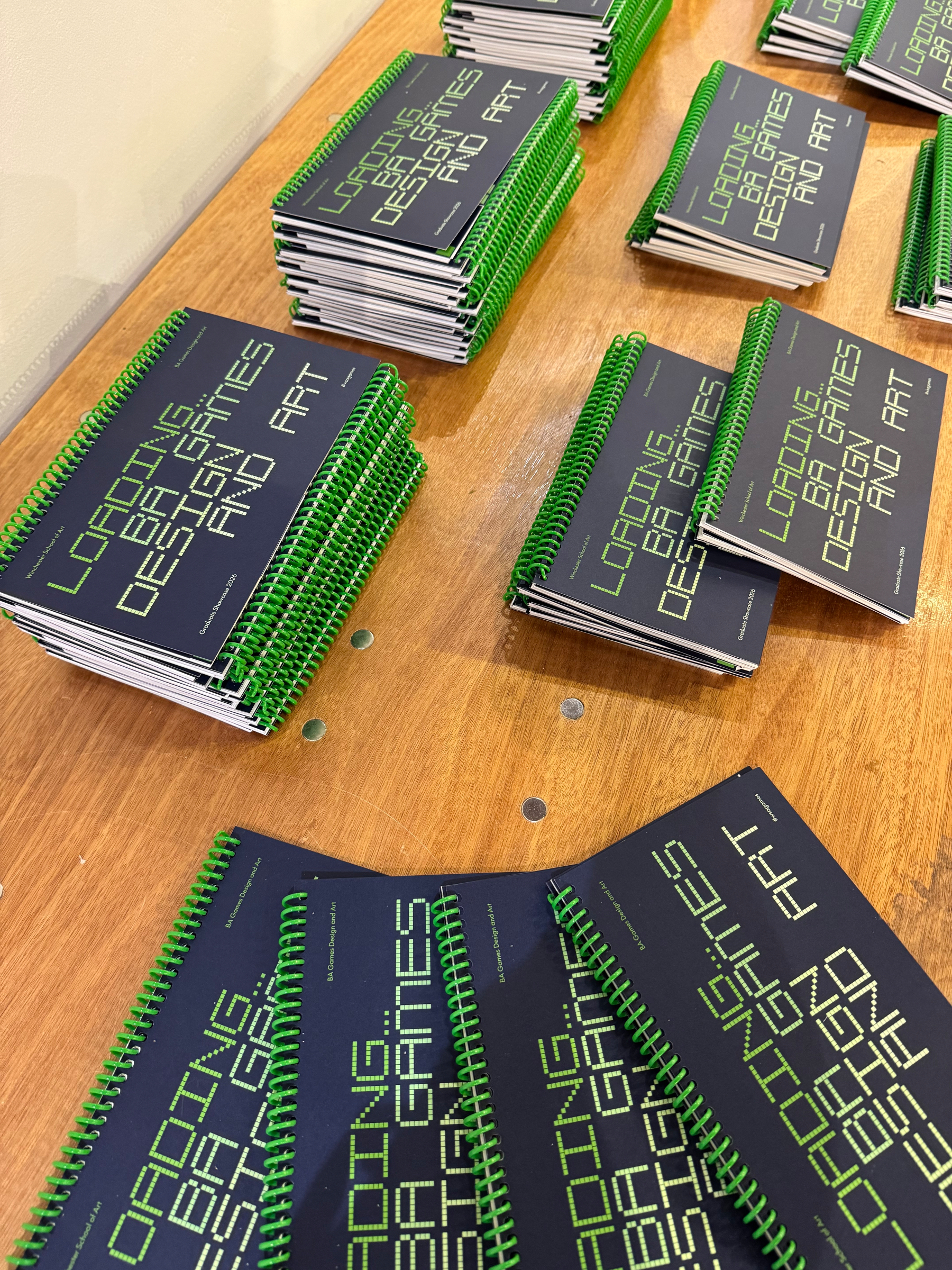 Stacks of spiral-bound notebooks with black covers and green text arranged on a wooden surface.