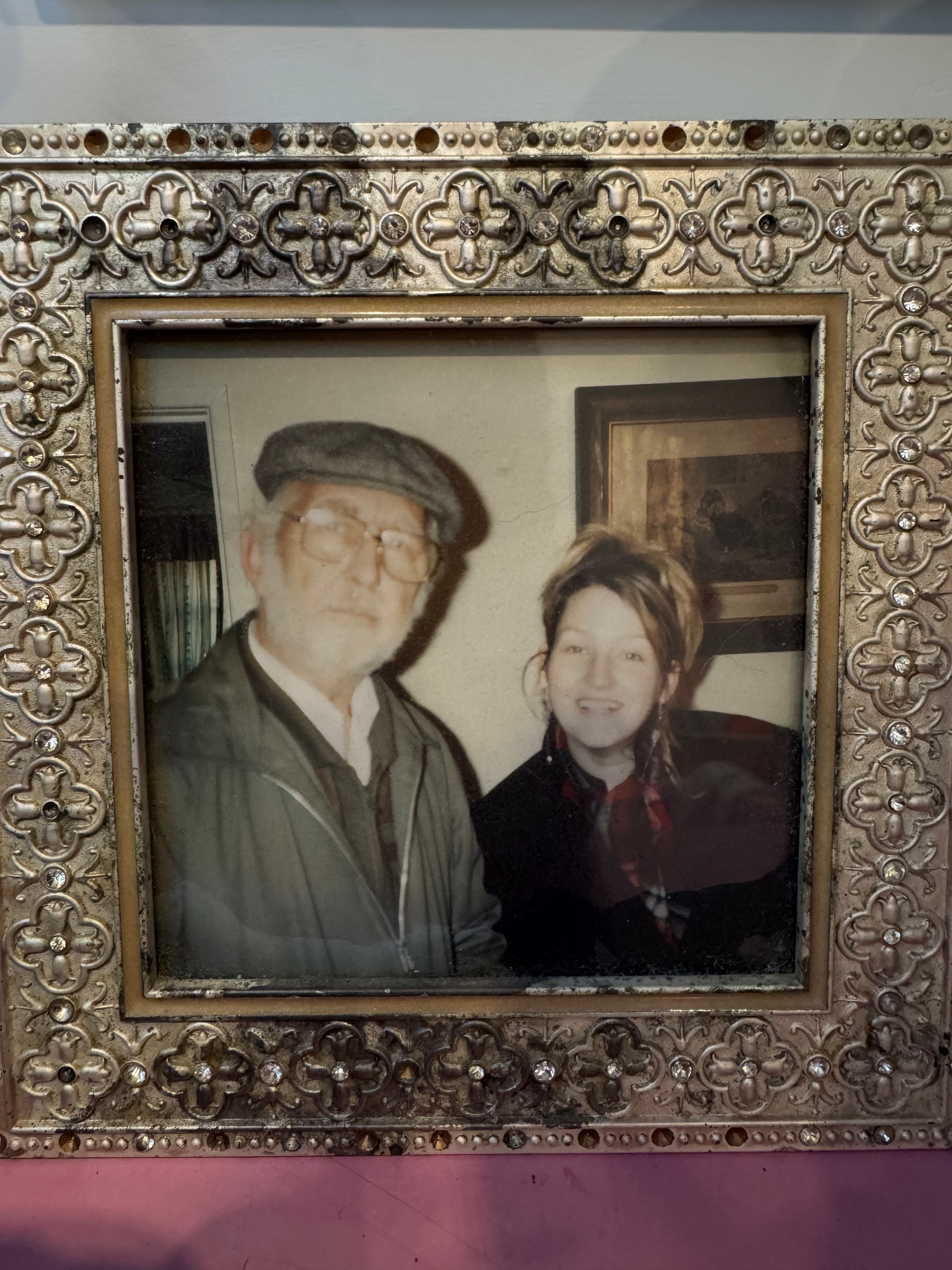 A framed photograph of two people, one wearing a flat cap and glasses, and the other smiling beside them.