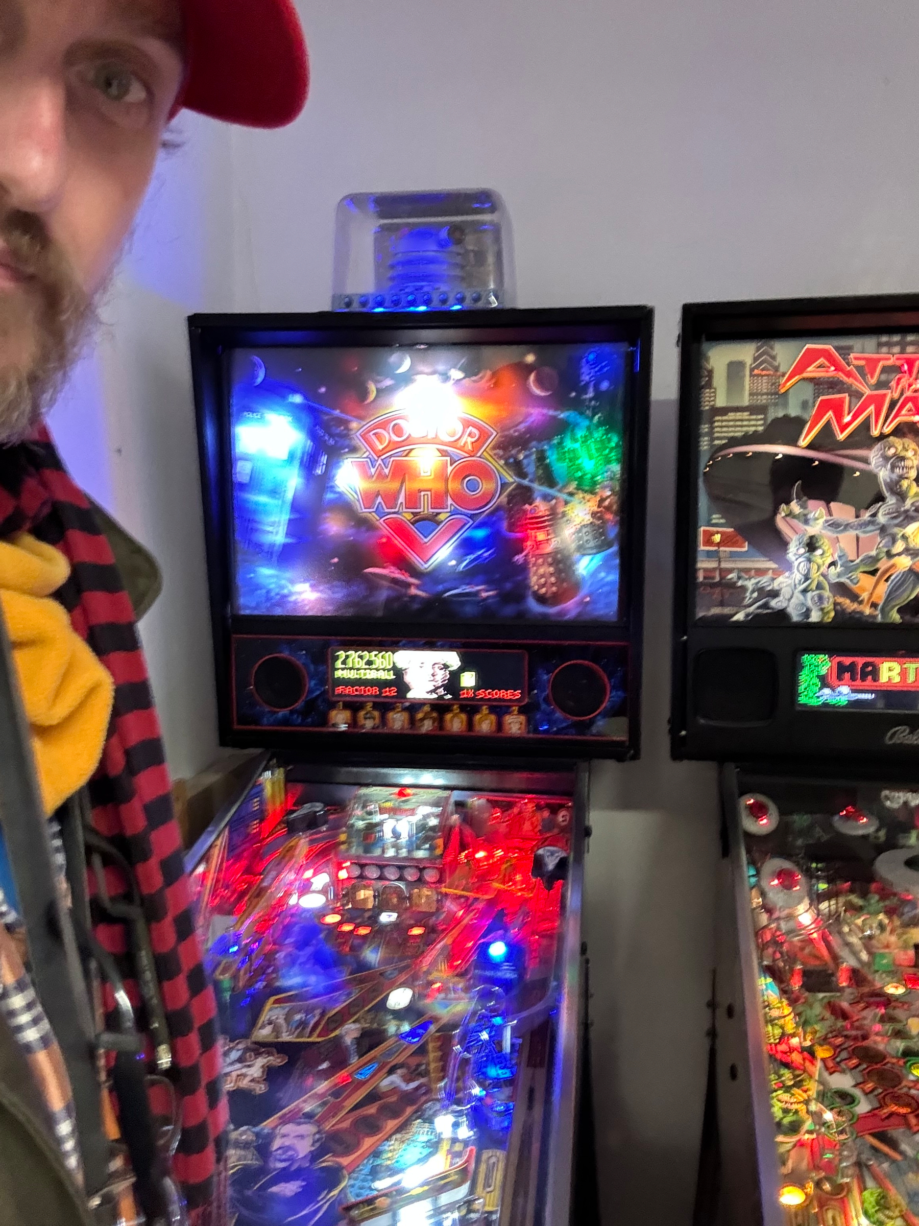 A person stands next to two pinball machines, one themed after Doctor Who.