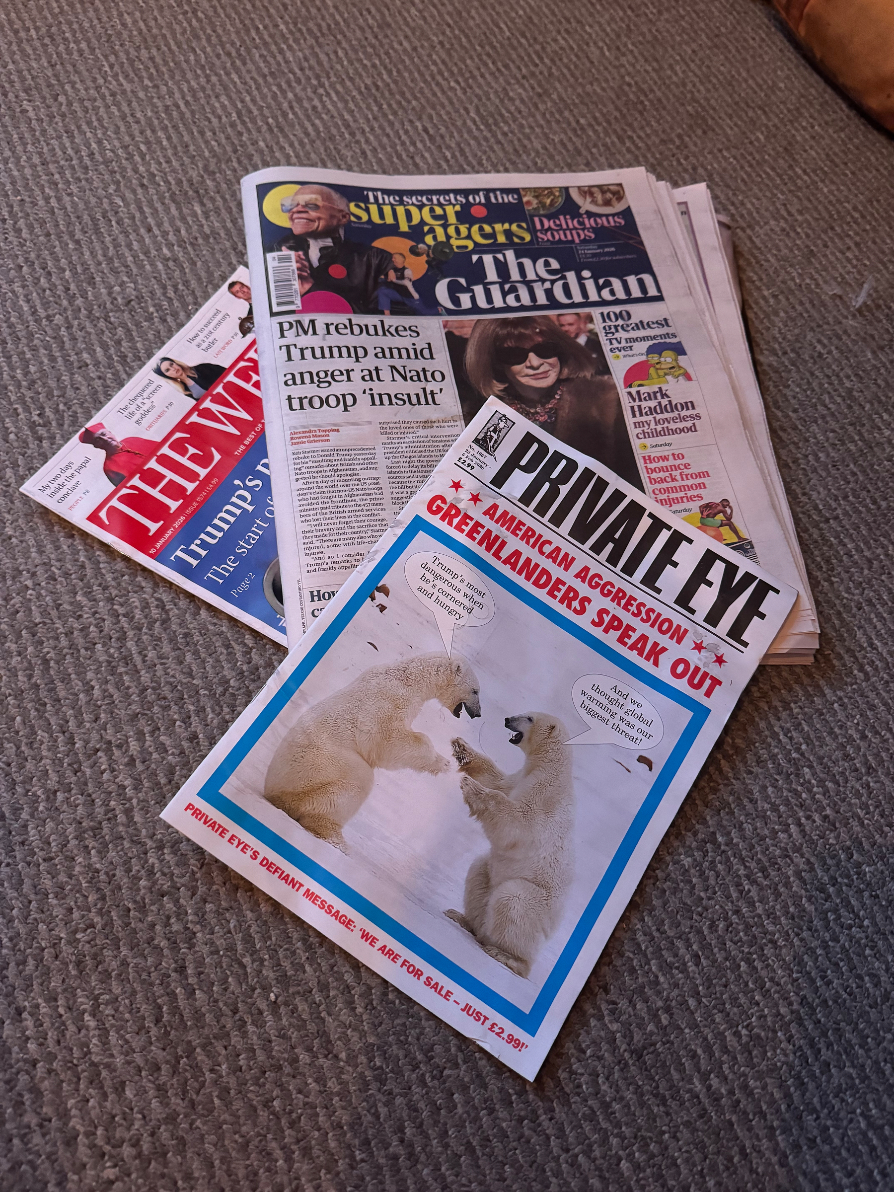 Several newspapers and magazines are scattered on a carpeted floor, including The Guardian and Private Eye.