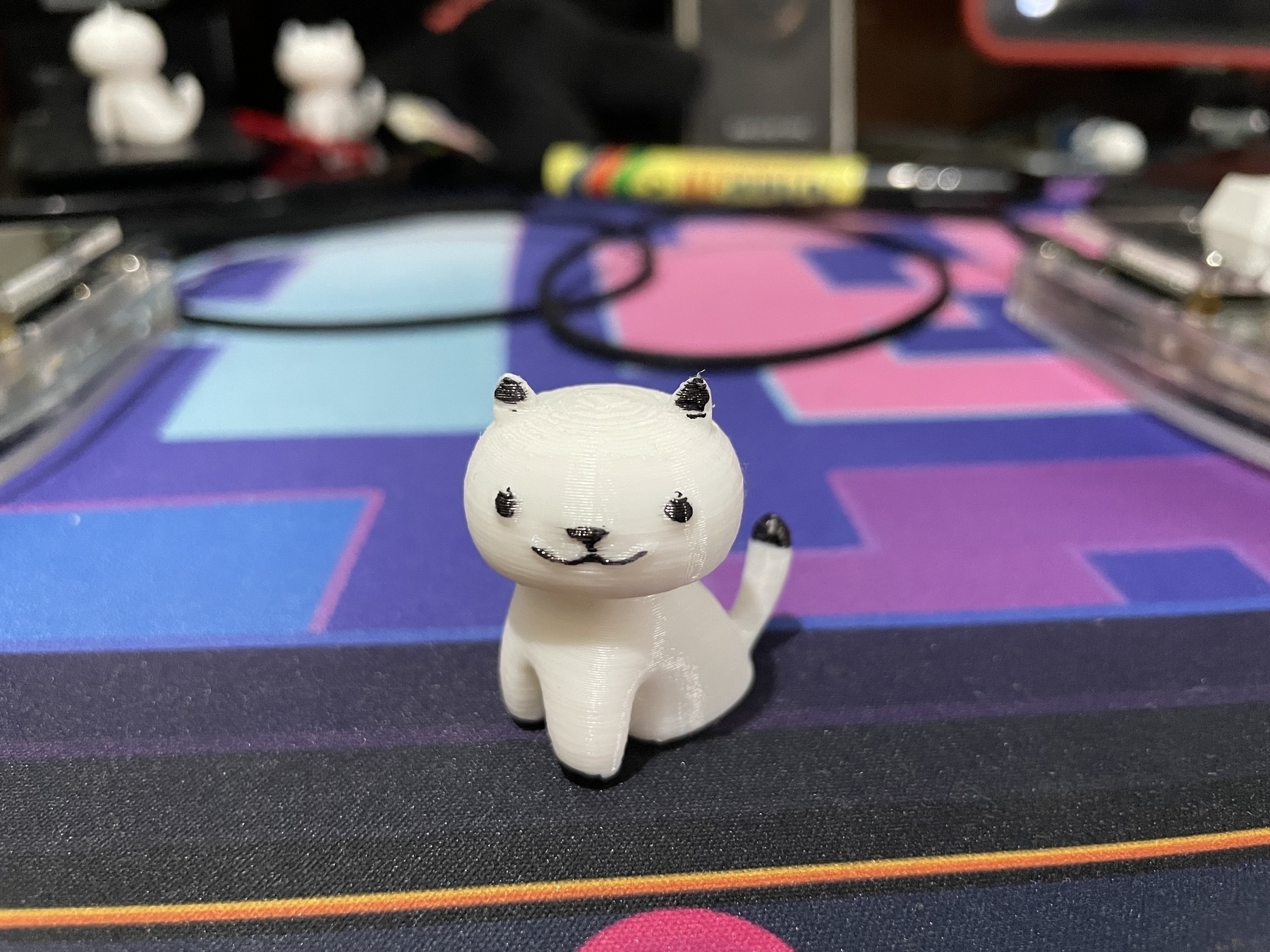 photo of a 3d-printed white cat with simplified features, like the cats from Neko Atsume. The eyes, ears, and tip of the tail are colored black to give the cat more character.