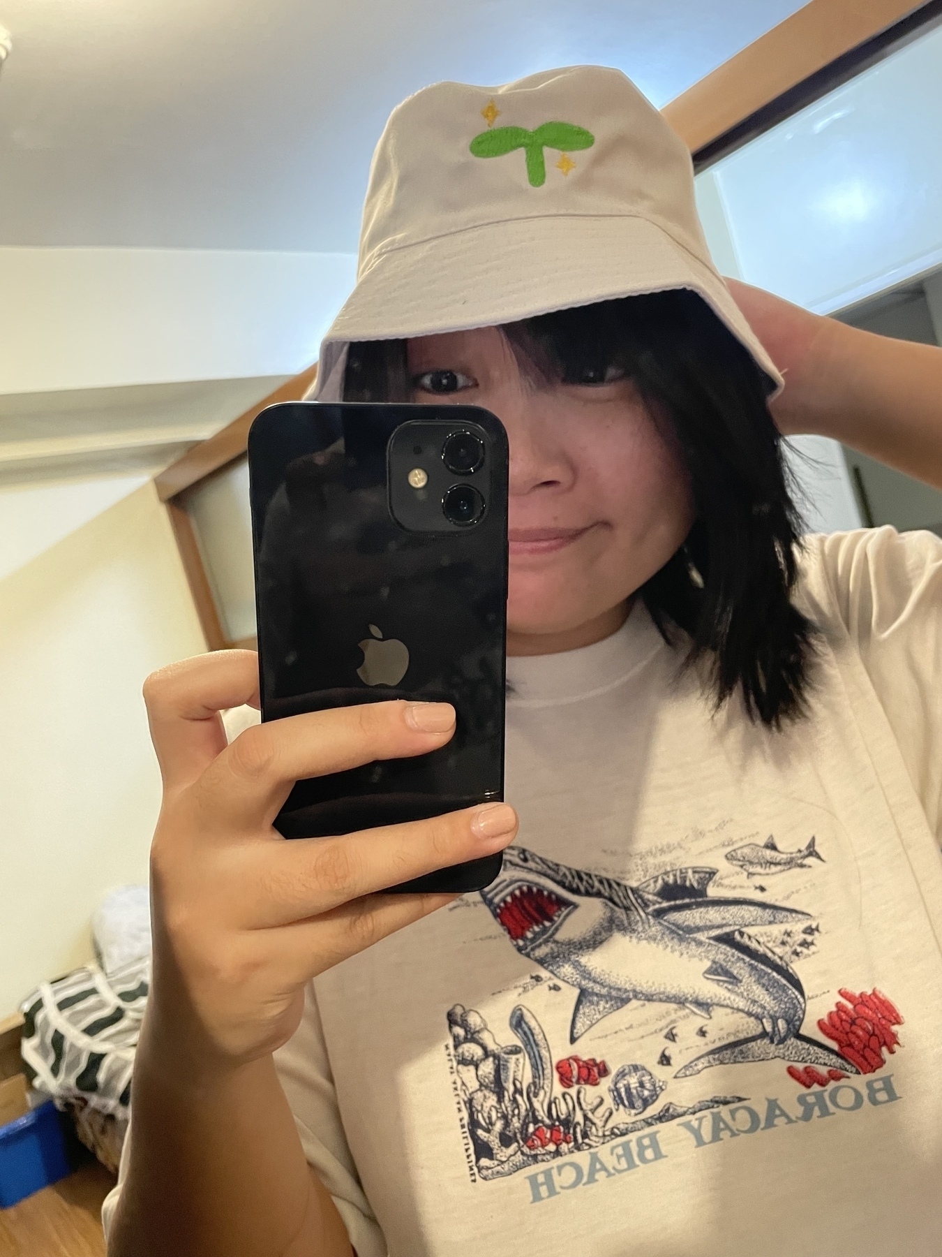 Mirror selfie of Chi wearing a white bucket hat with a green sprout icon on it, which usually signifies a new adventurer or new account in FFXIV.