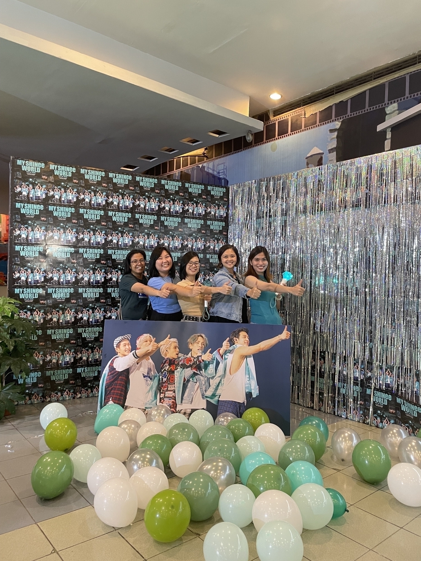 Group photo of Marie, Chi, Cathylou, Karen, and Joan behind a big photo stand of the SHINee members and mimicking the pose of Onew, Taemin, Jonghyun, Key, and Minho showing a thumbs up to the right side of the area. A tiled poster of My SHINee World is seen as a backdrop, with lots of balloons scattered in the foreground.