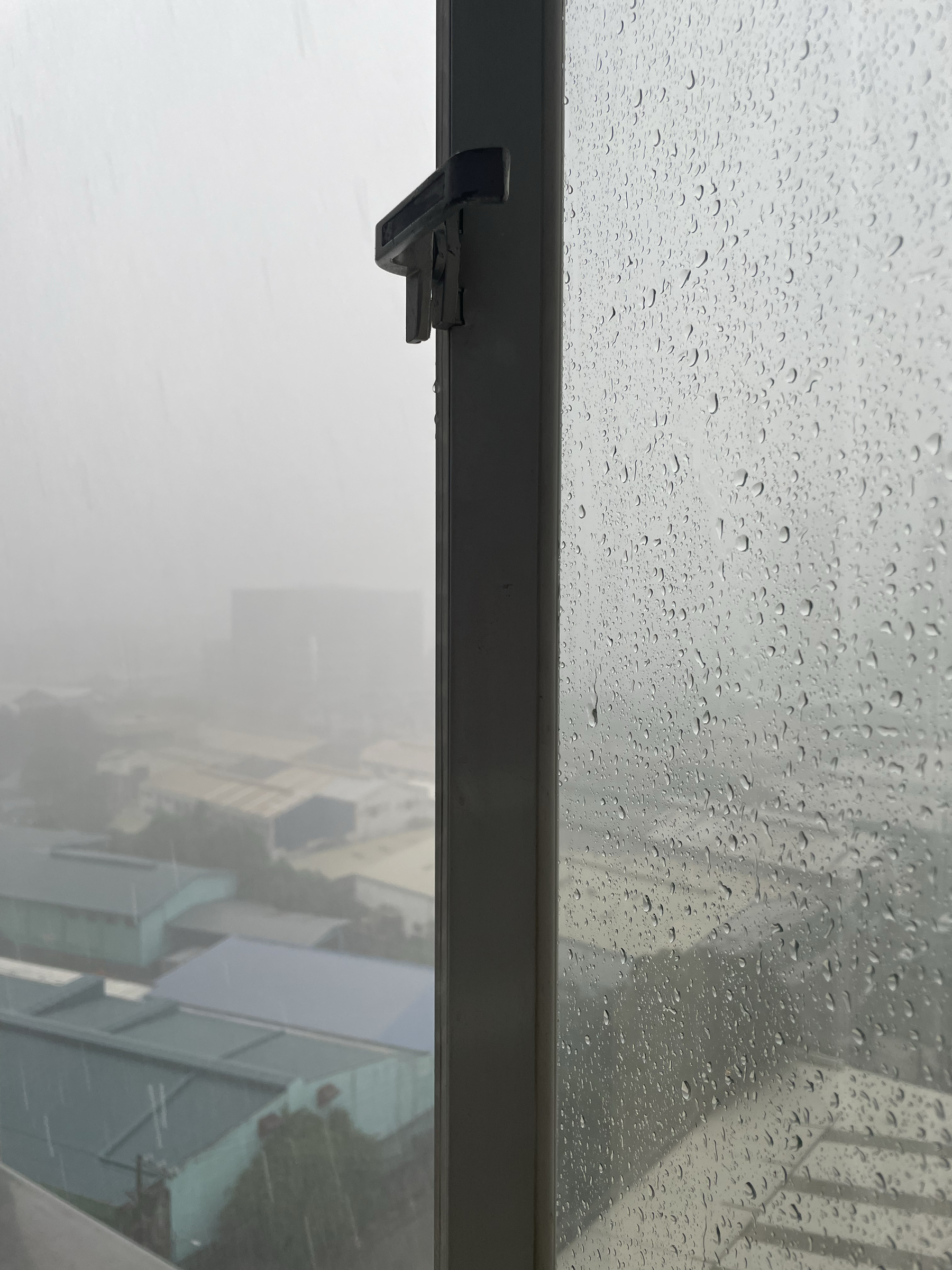 photo of a half opened window with lots of raindrops on its surface, showing the torrential rain outside providing low visibility