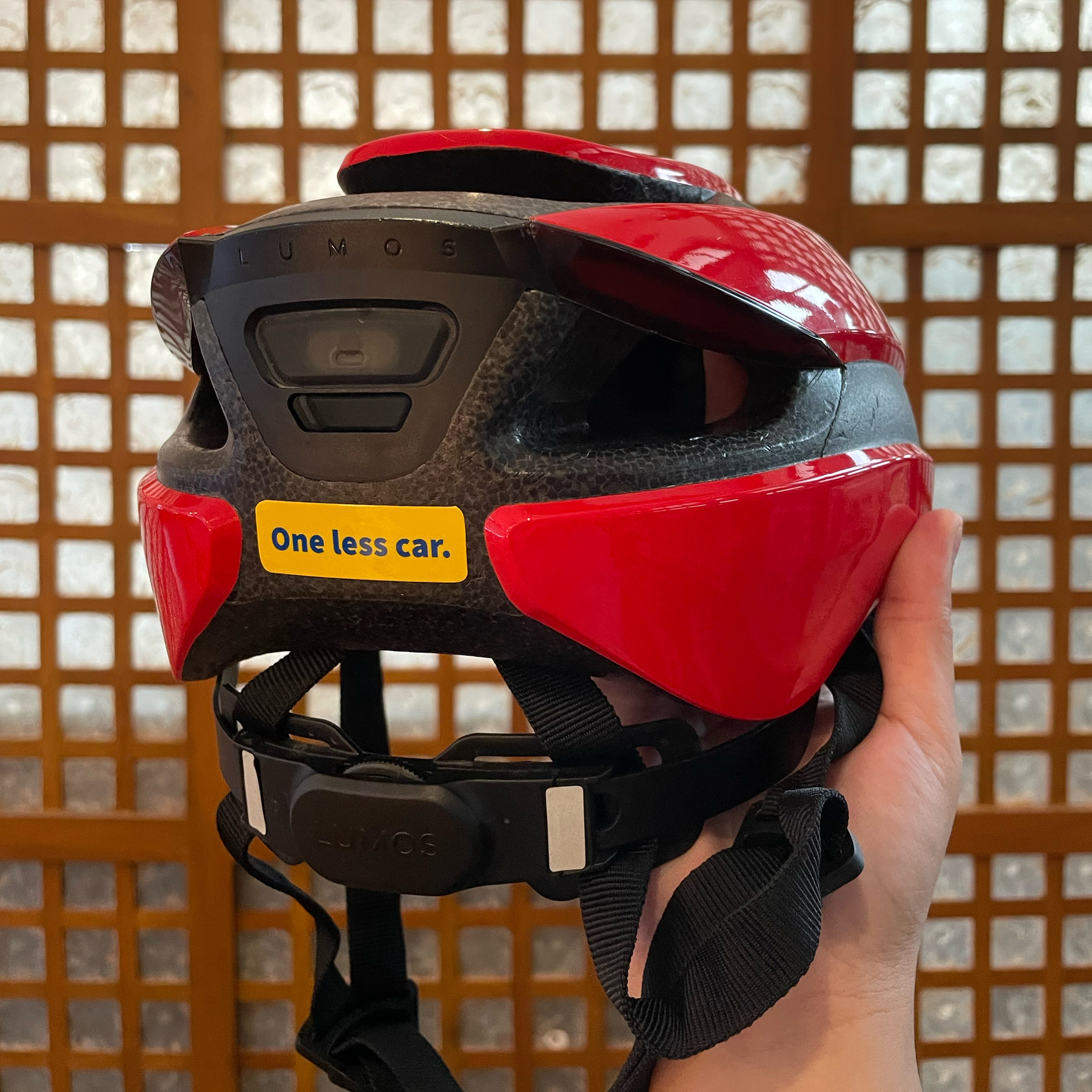 photo of the back of a red Lumos helmet, with the sticker “One less car” shown