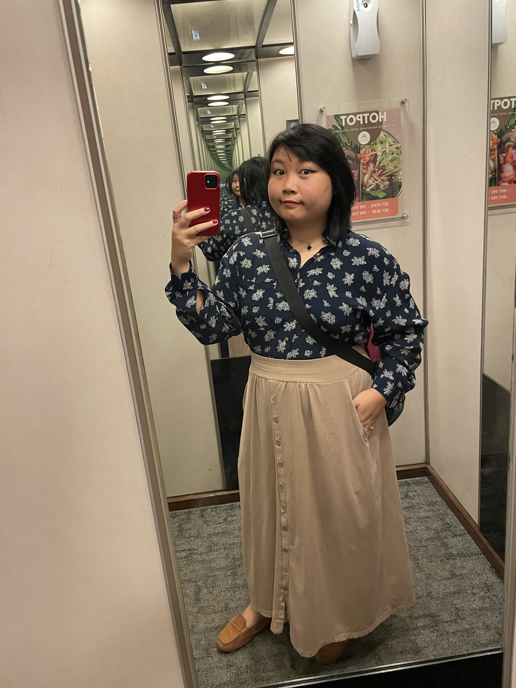 Mirror elevator selfie of Chi showing her current outfit for the day: a long-sleeved blue polo shirt with a leaves pattern tucked in a long beige skirt.
