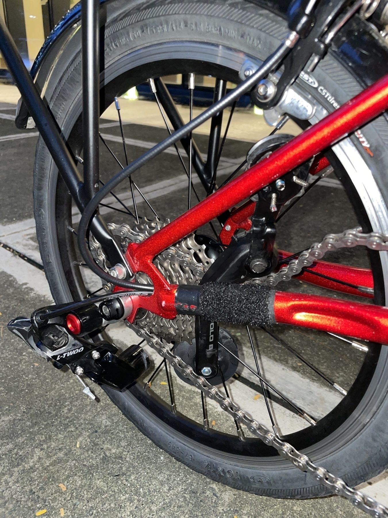Chi’s folded bike, focusing on the place where the rear derailleur and gears are. The chain tensioner is broken, and the bike’s chain is not in its tensed state anymore.