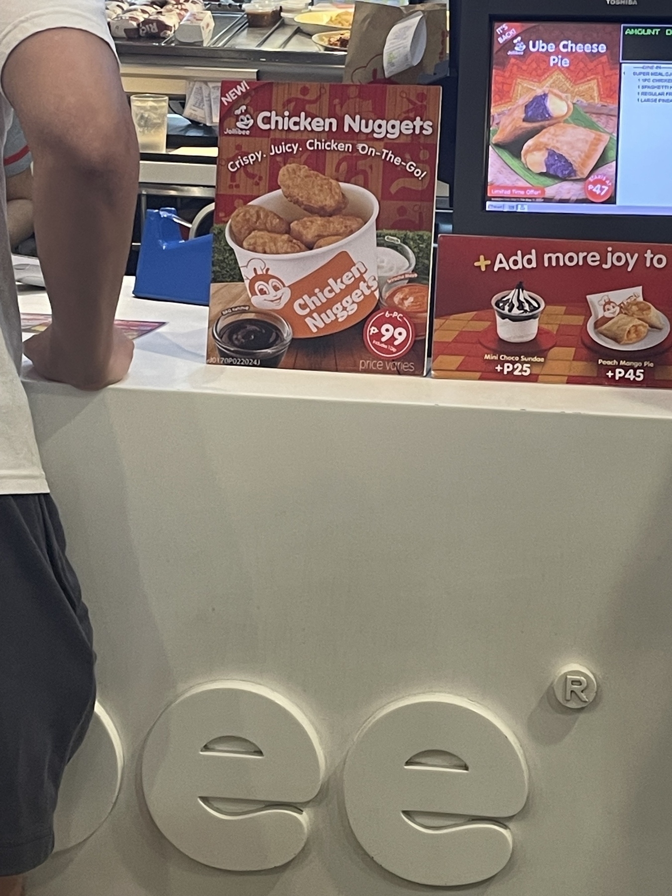 A promotional poster from Jollibee in front of their cashier registers sharing that Chicken Nuggets is now available.