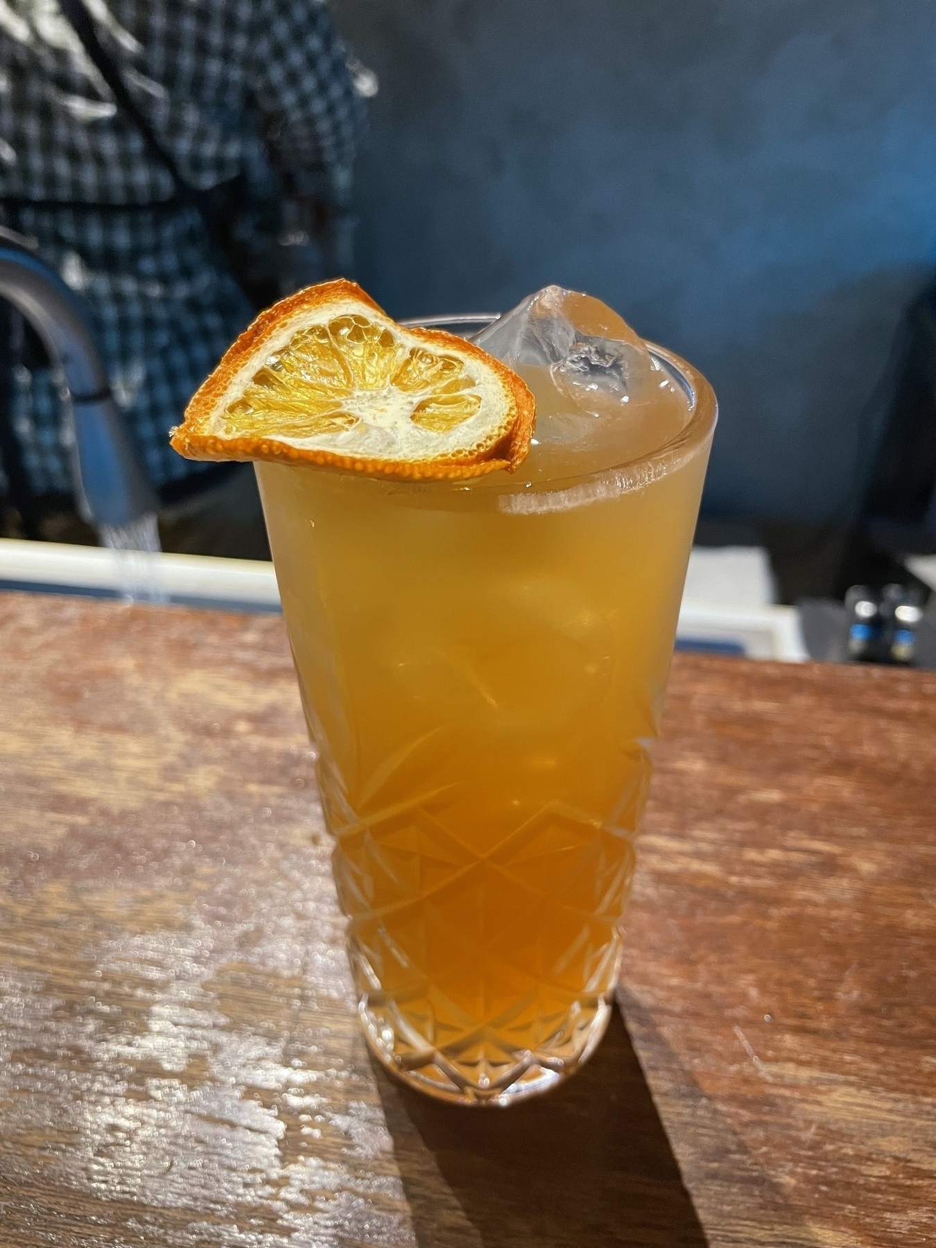 A mixed orange cocktail in a tall glass with a dried orange as a garnish, with ice in the drink as well.