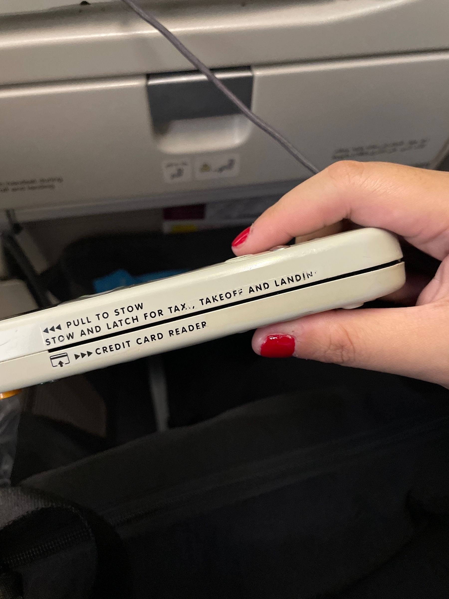 A credit card reader seen on the side of the remote available for in-flight entertainment in an airplane. The text above the card slot reads: "Pull to Stow | Stow and Latch for taxi, takeoff and landing"
