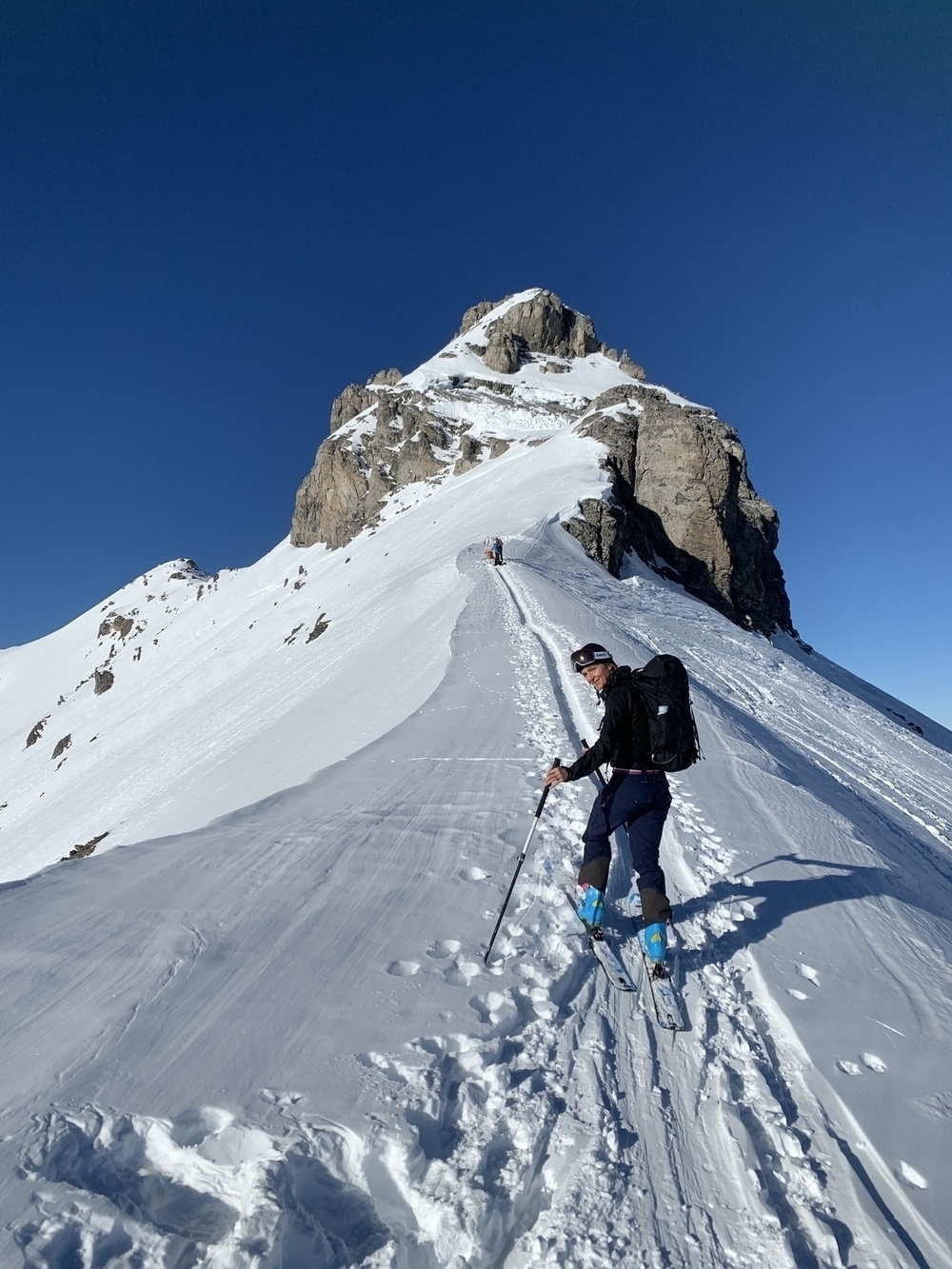 A person is hiking up a snowy mountain trail under a clear blue sky.