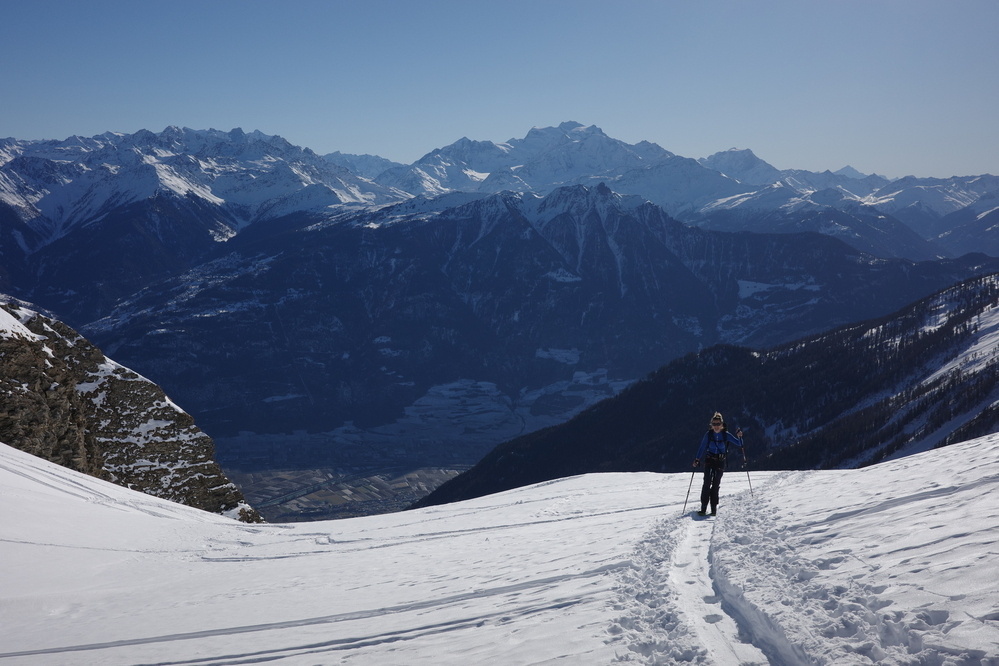 A person is skiing on a snowy mountain slope with a vast range of mountains in the background.