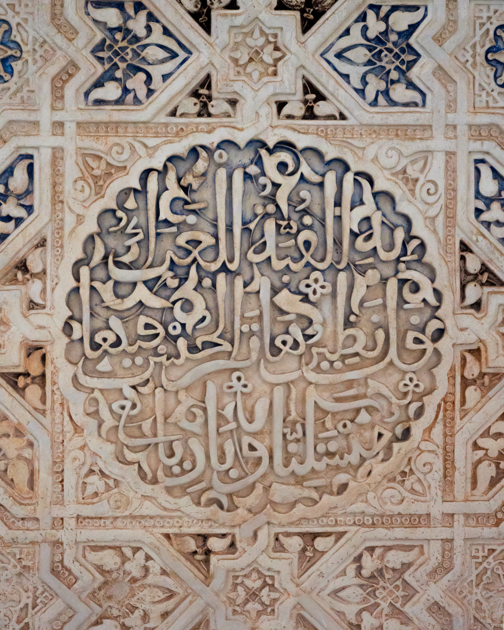 An intricate wall decoration with a mix of patterns and Arabic text. You can see remnants of ancient paint that has been faded or removed with time. 