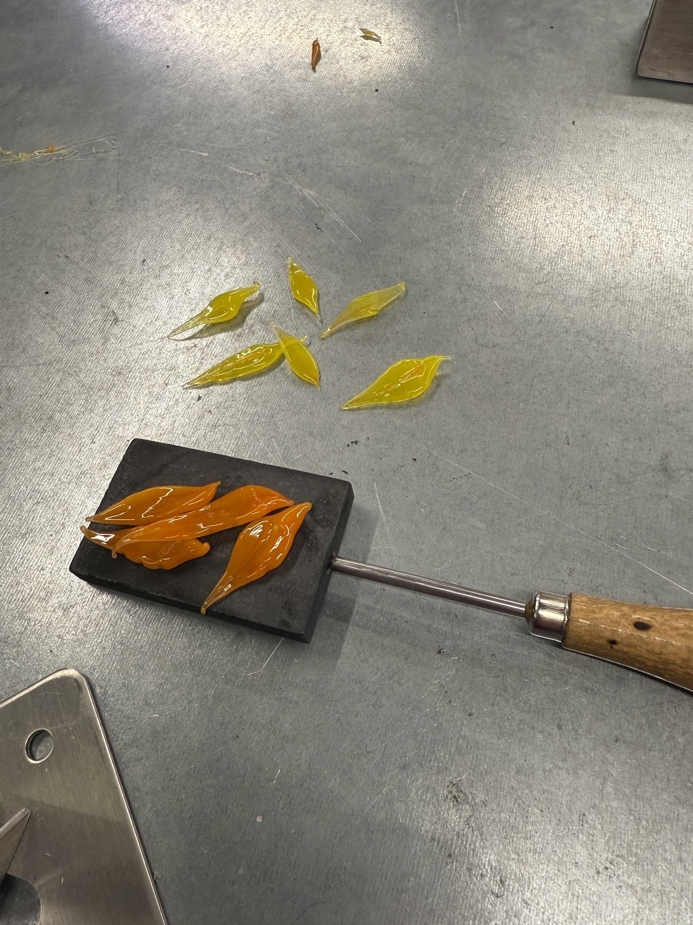 Yellow and orange pointed glass leaves on a metal table and graphite marver