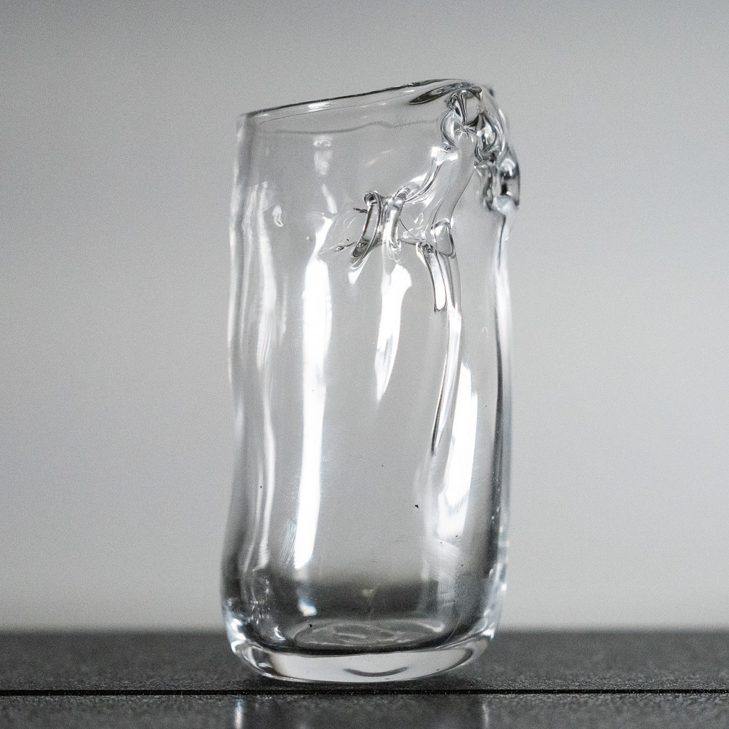 A tall narrow cup, it has weird folds of glass caused by overheating thin glass during the blowing process.