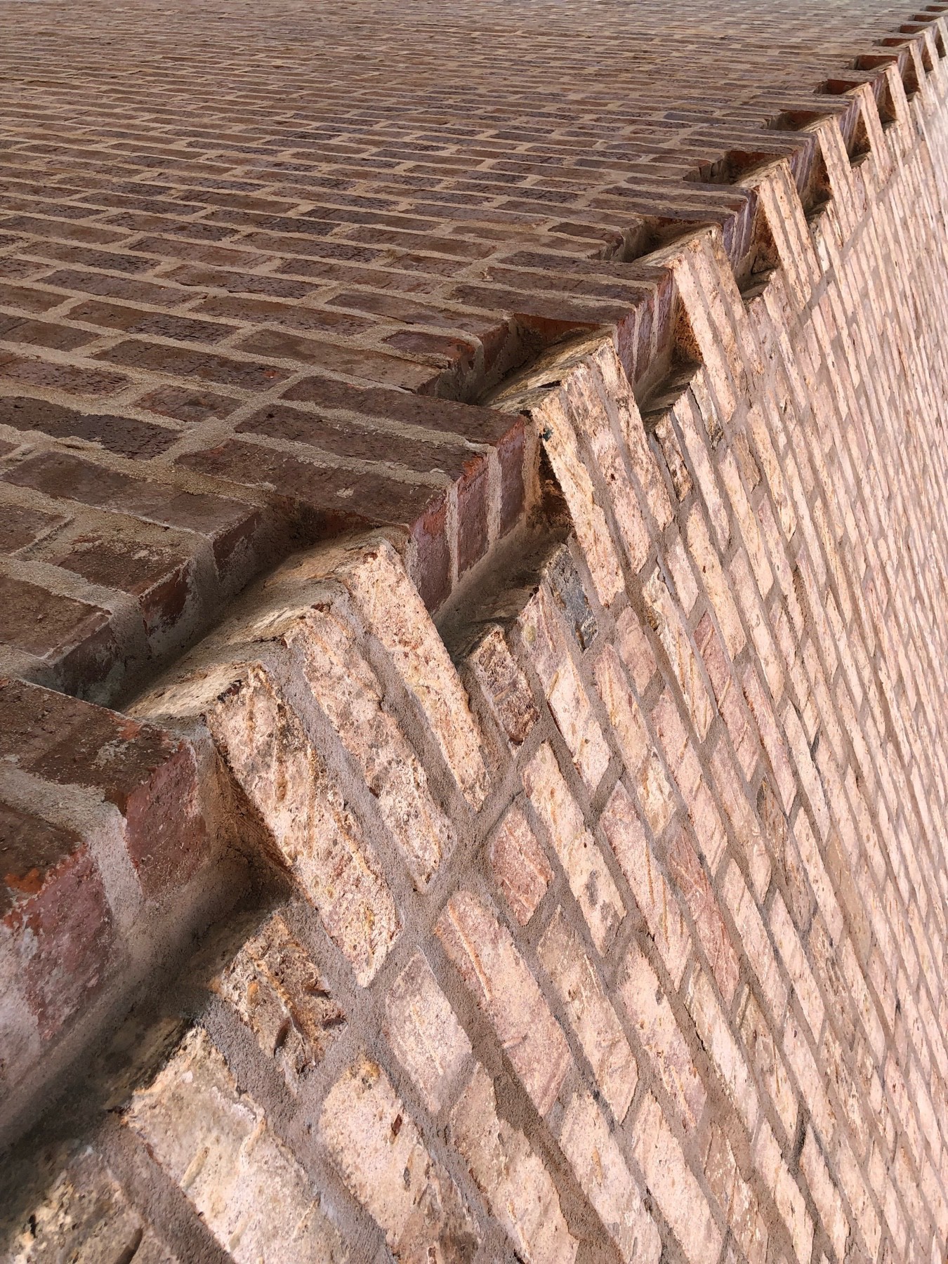 Two brick walls joined together in a teeth-like manner.  The joint is angled from bottom left to top right, and the wall on the right is a lighter shade of red than the left.