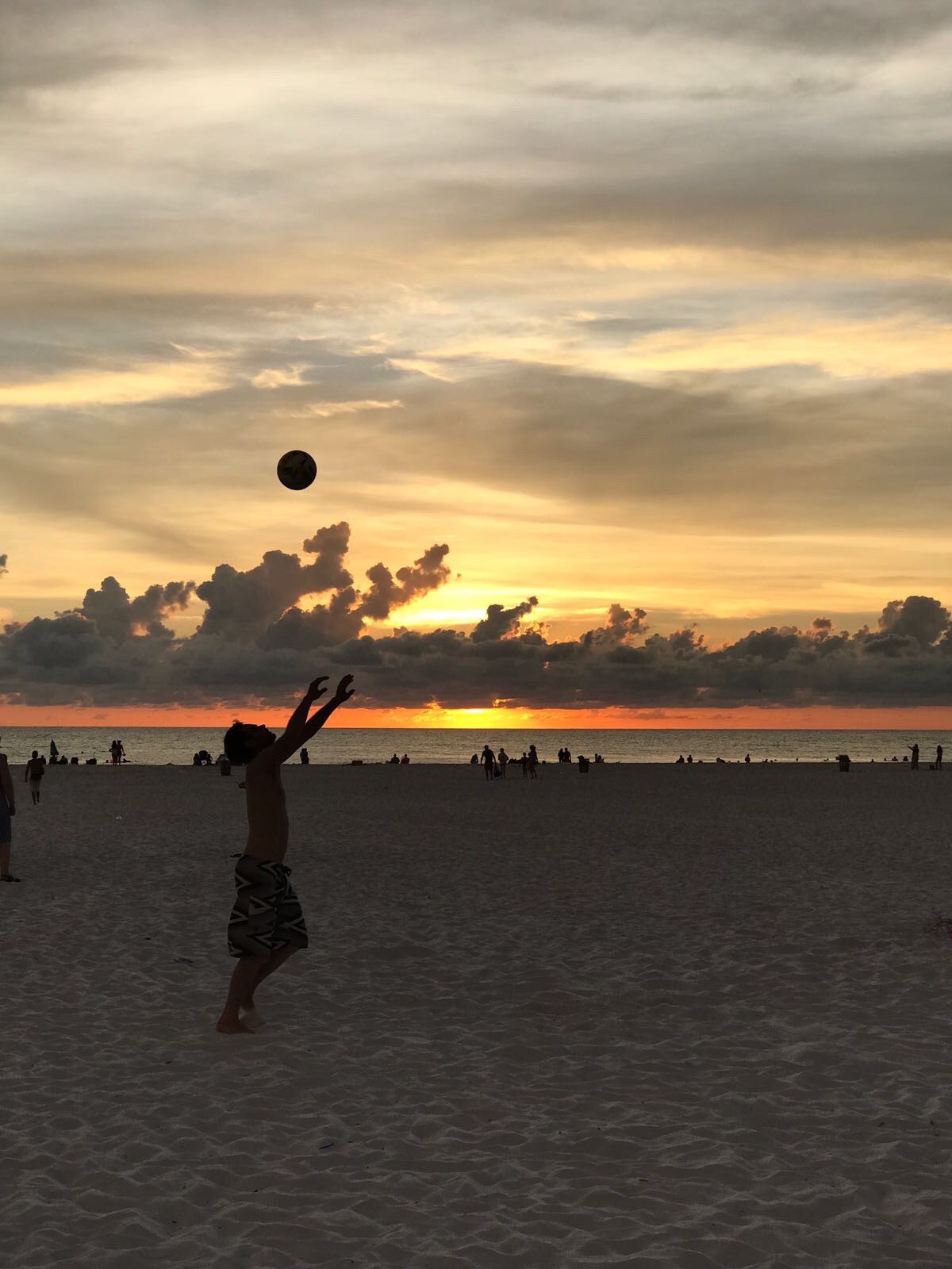 A sunset silhouette of a young male volleyball player tossing the volleyball high above his head