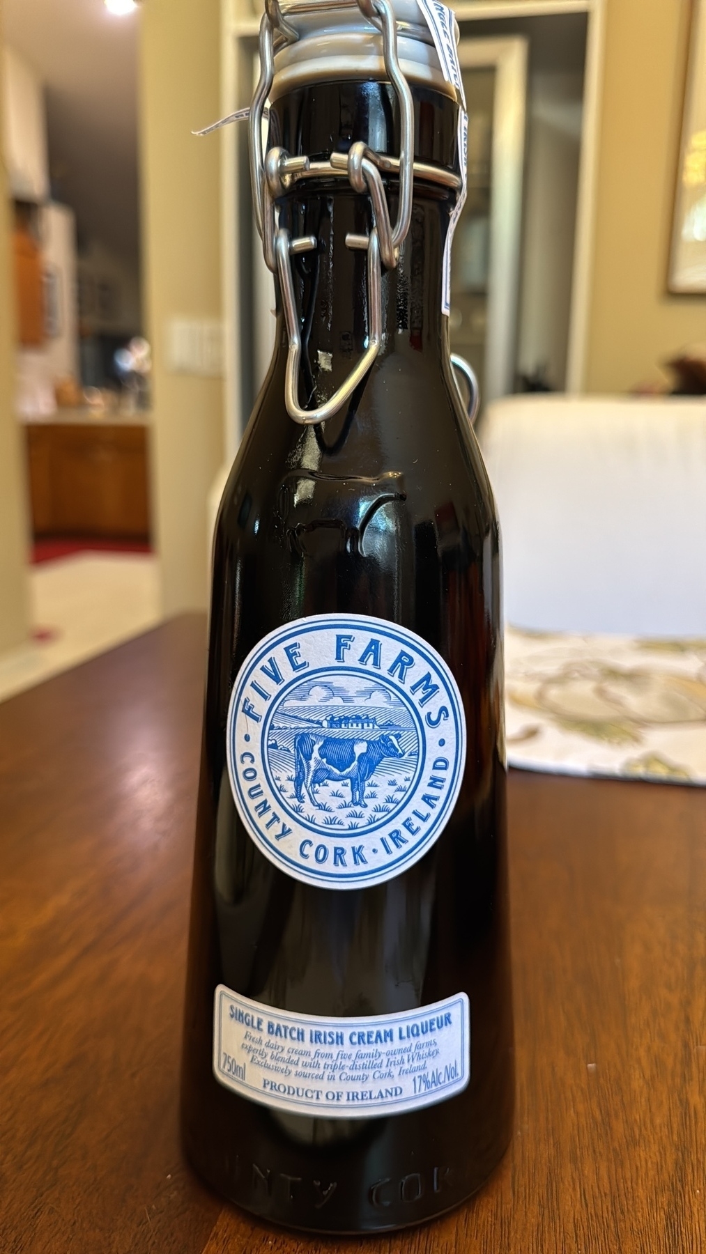 A shot of a bottle of Irish cream sitting on a wooden table. The label says “Five Farms County Cork Ireland and the lower label says, “Single batch Irish cream liqueur - fresh dairy cream from five family-owned farms expertly blended with triple-distilled Irish whiskey exclusively sourced in County Cork, Ireland — 750 ml Product of Ireland — 17% alc by volume”