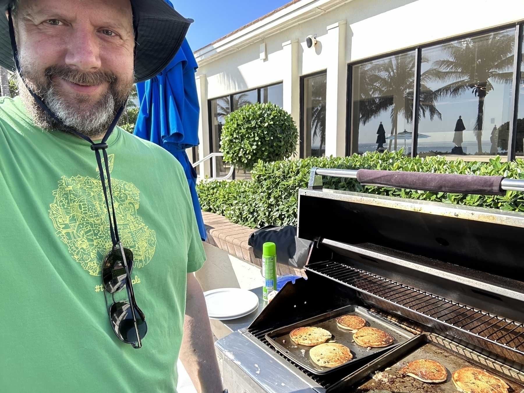 Me at a grill cooking pancakes. palm trees and the ocean reflected in clubhouse windows.