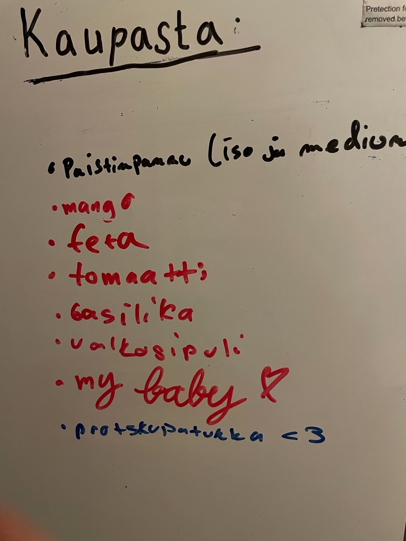 shopping list in Finnish on a white board: mango, feta, tomaatti, basilika etc.