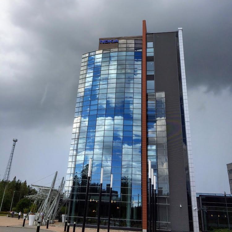 glass facade of building reflecting blue skies, thunder storm rising behind the building