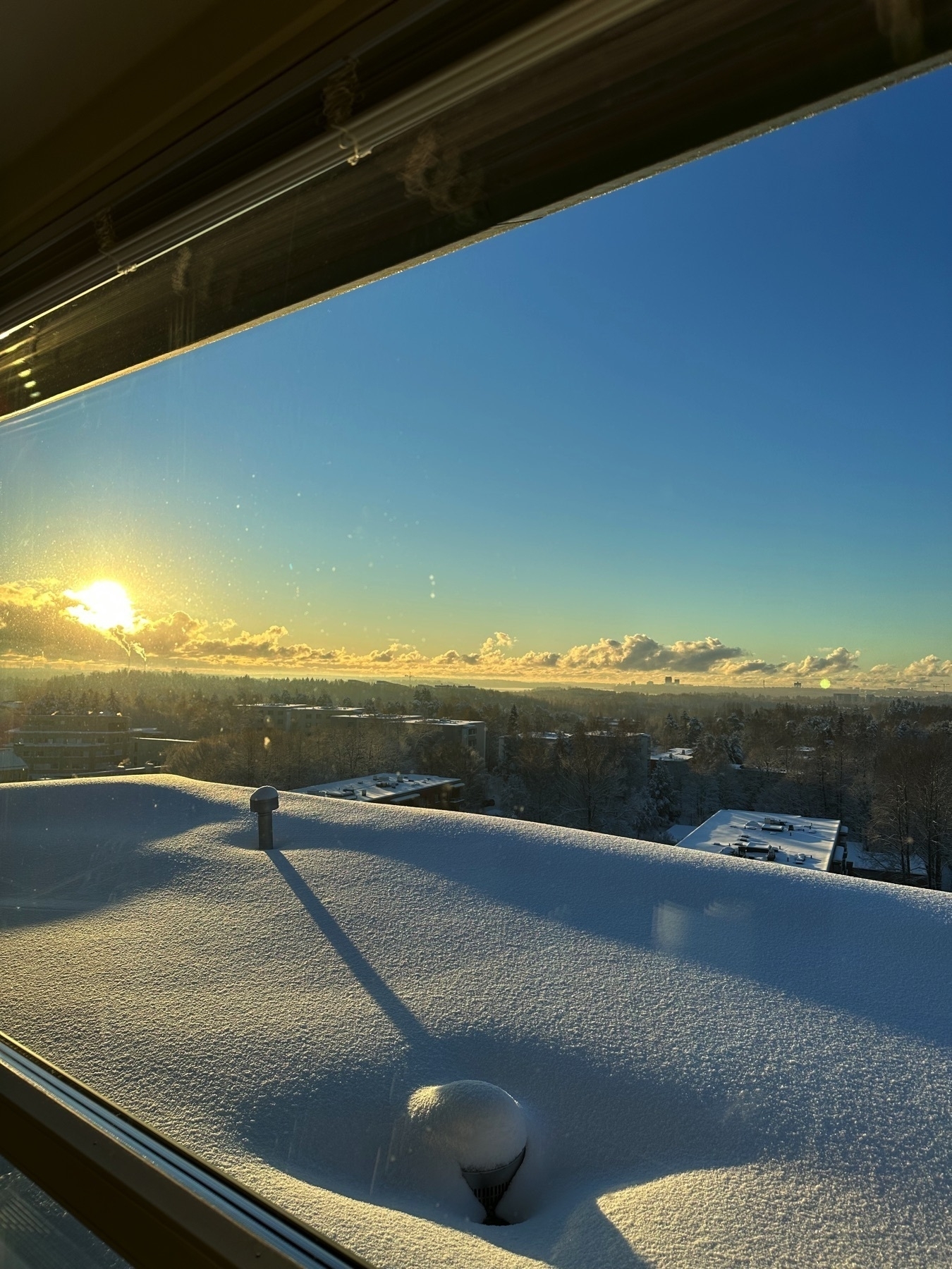 snowy rooftop opening over buildings, forest, open sky and sun  
