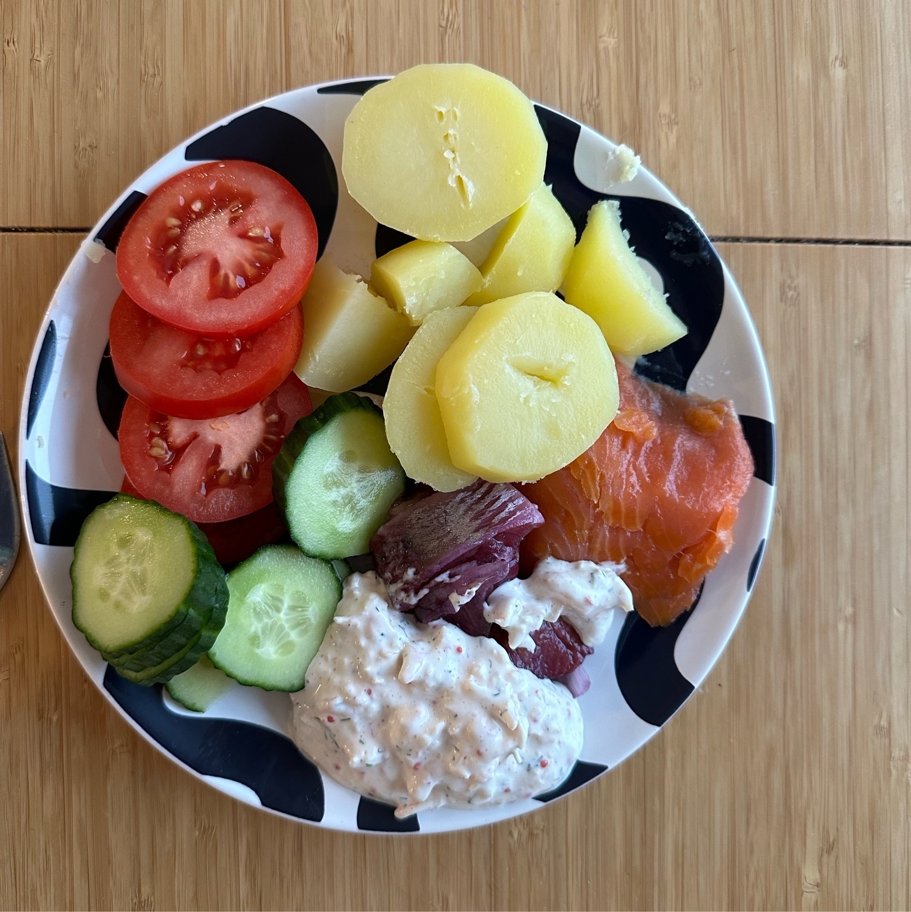 small plate containing boiled potatoes, cucumbers, tomato, small slices of pickled herring, smoked salmon and prawn salad