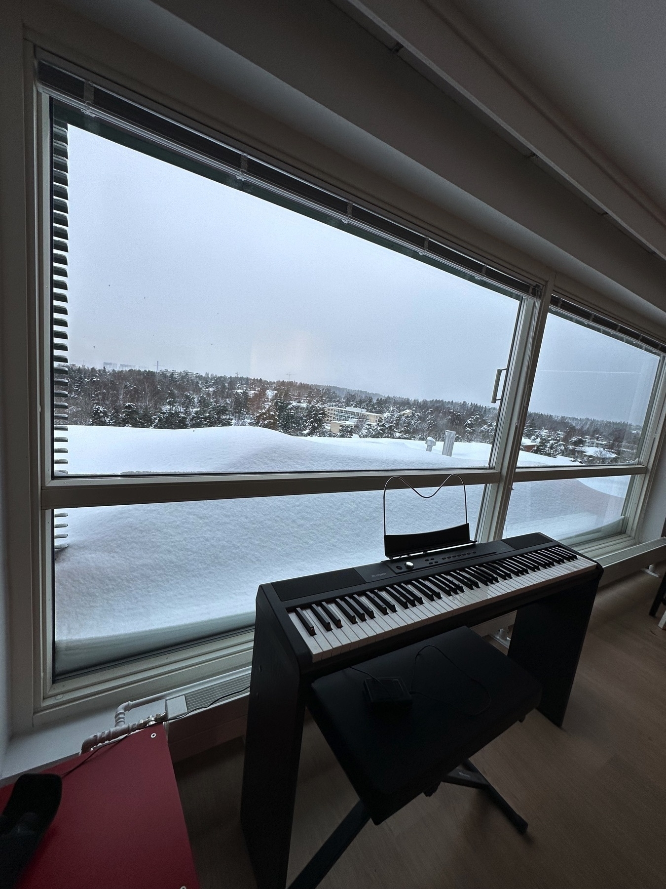A three feet/one meter tall pile of packed snow outside of a window. Electric piano in front of the window
