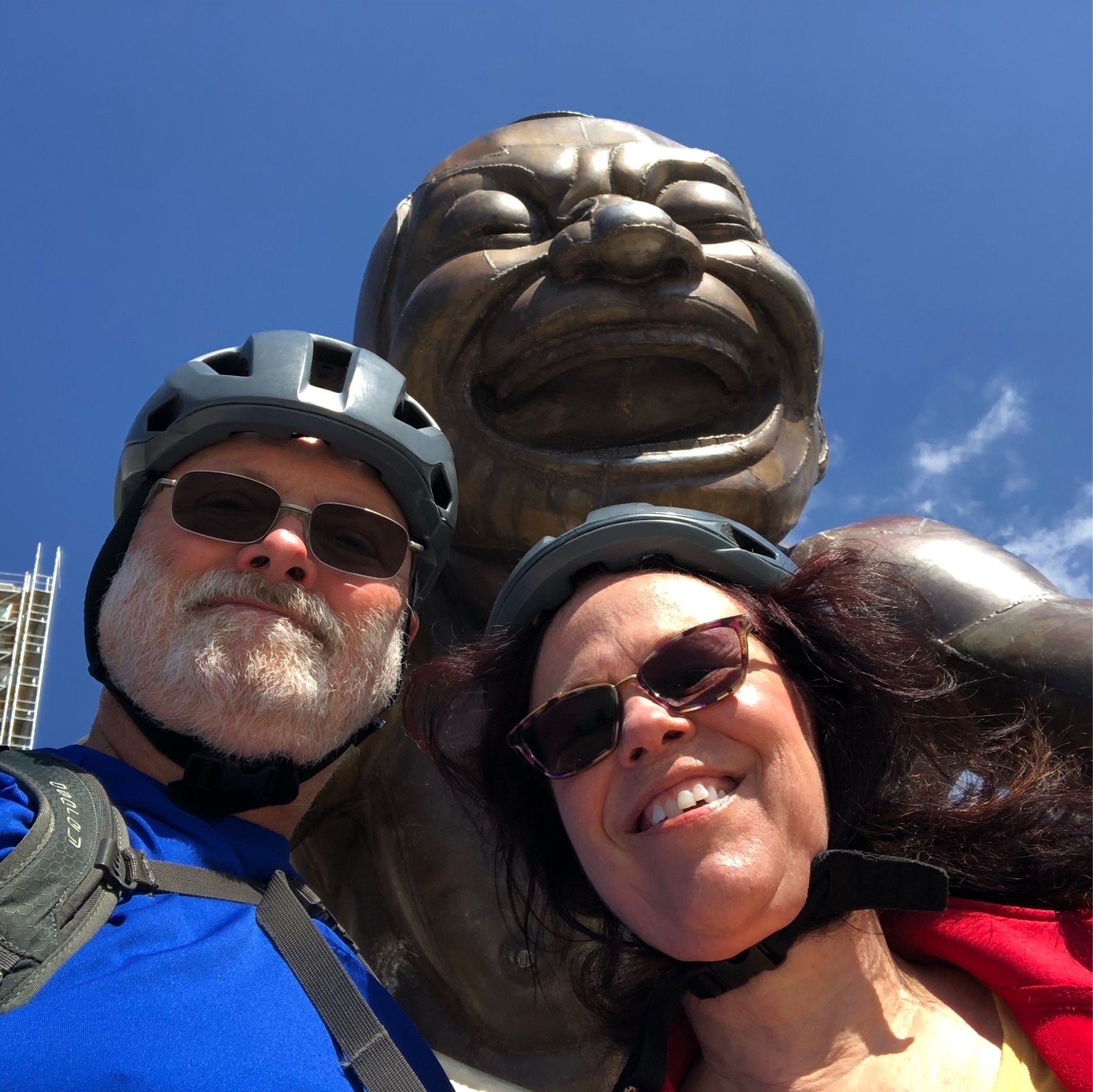 two people in bicycle helmets in front of bronze statue of man laughing 