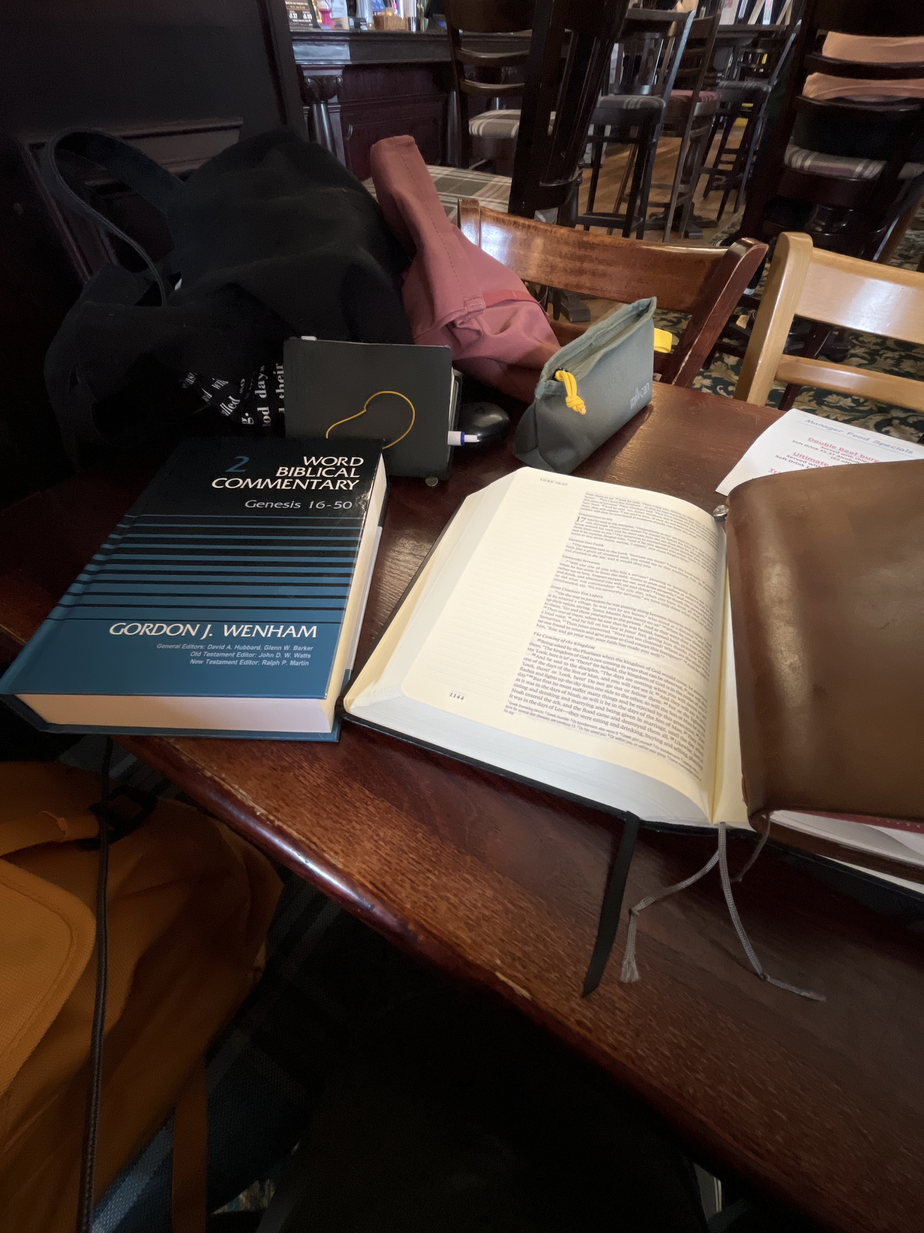 A pub table covered with books (the Bible and Gordon Wenham’s commentary on Genesis) and notebooks (Traveler’s Notebook in camel brown).