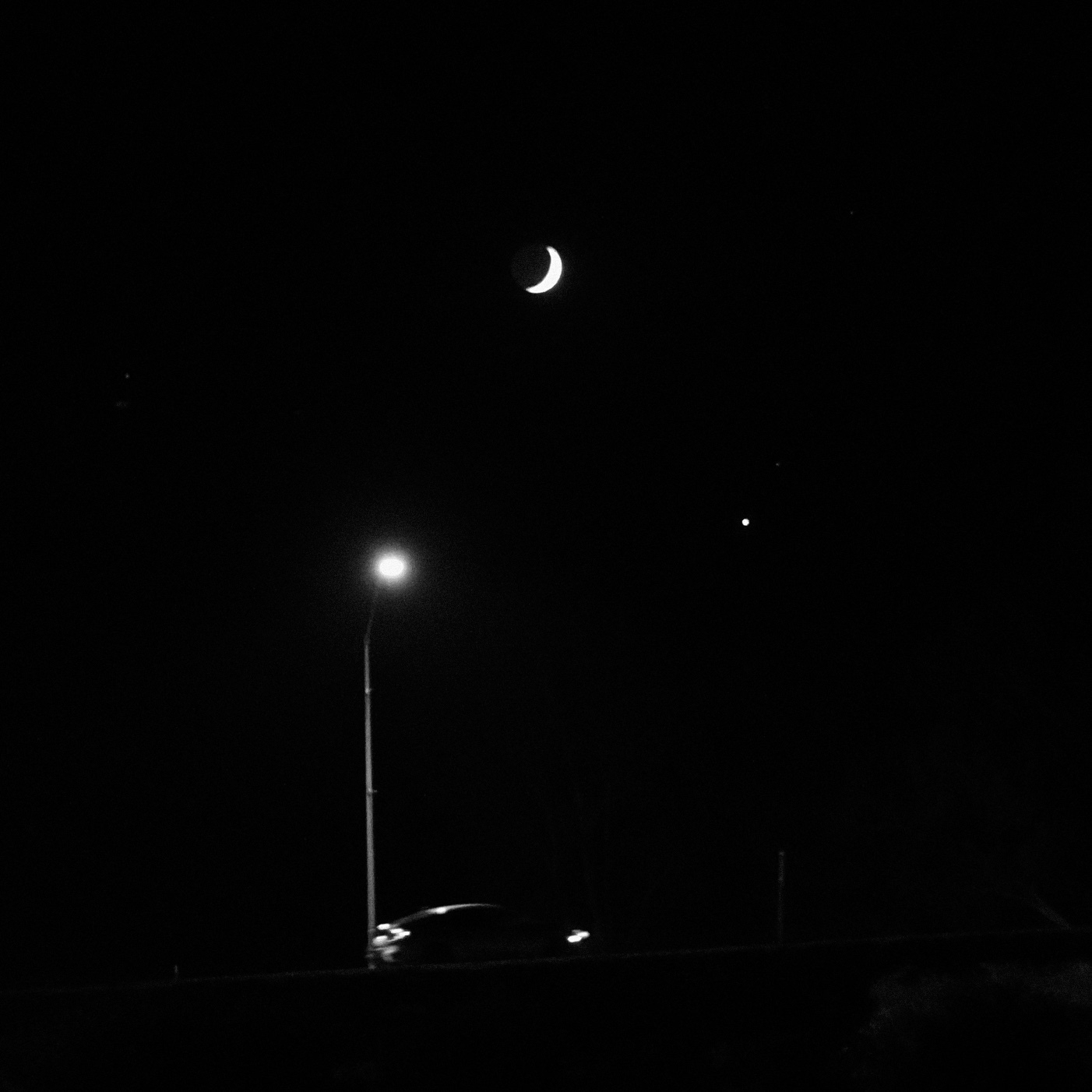 waxing crescent moon, venus, street light, and a car driving up a bridge. black and white photo.