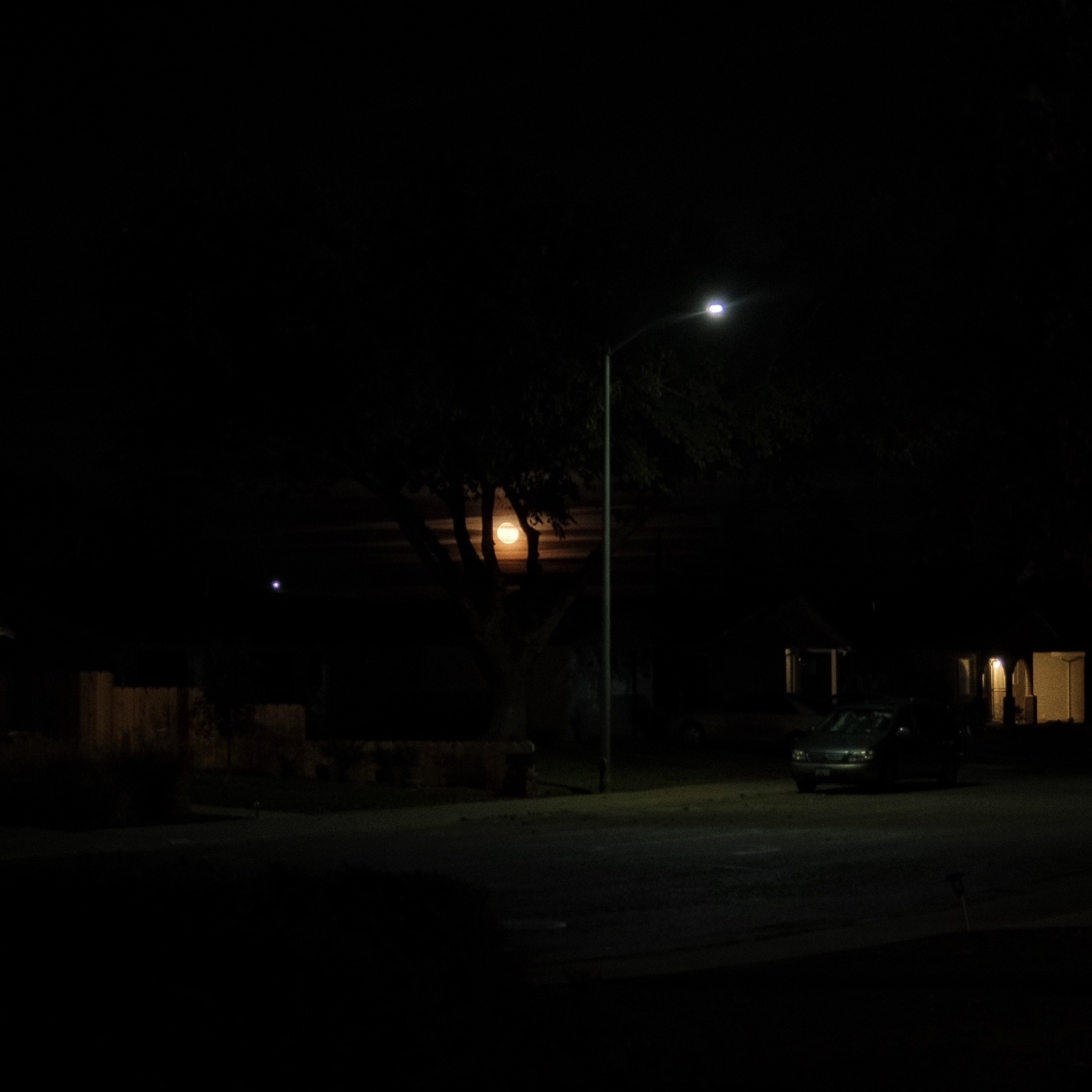 Orangish moonrise over houses on a dark street.