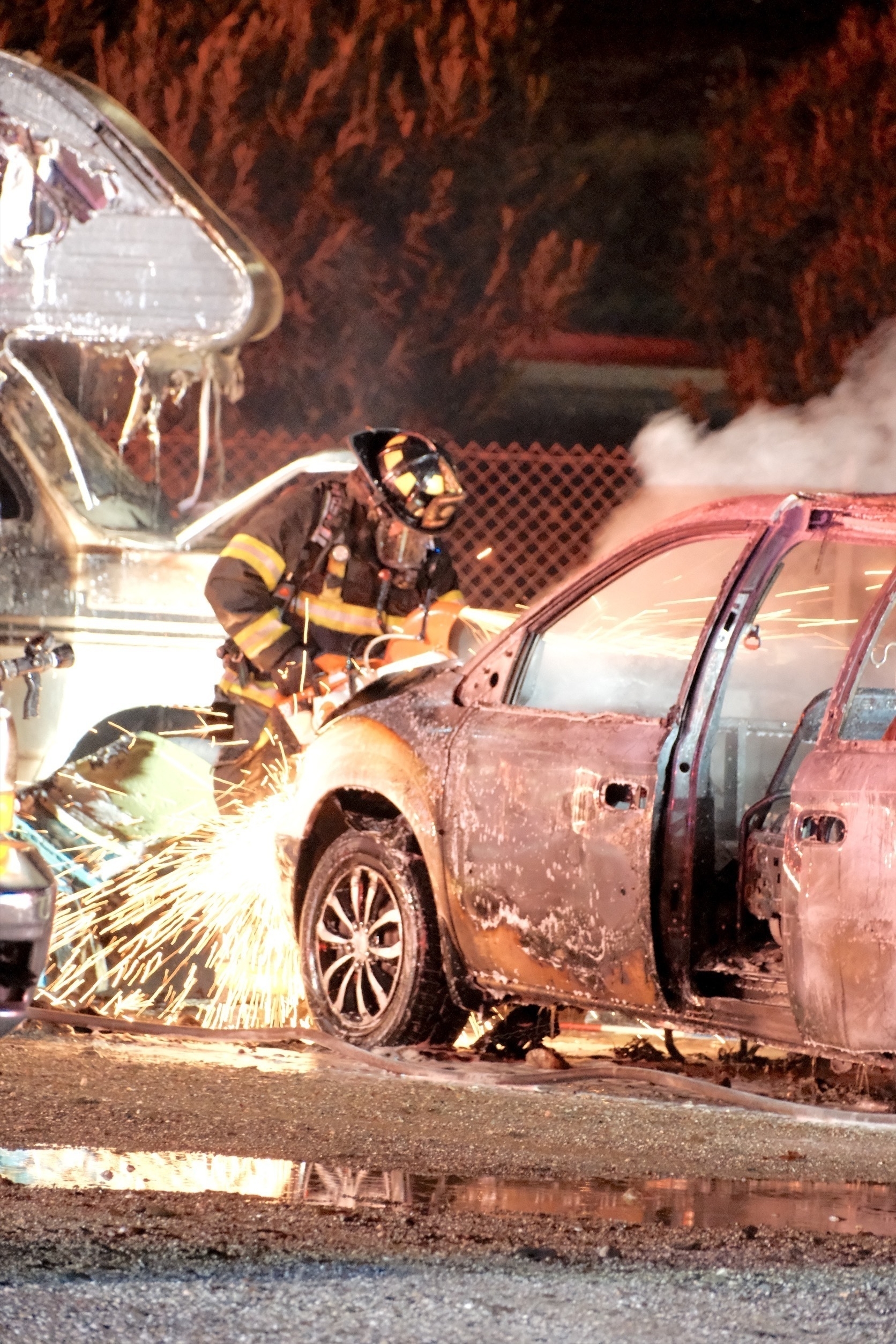 Sparks fly as a fire fighter cuts open the hood in efforts to make the burning vehicle safe.