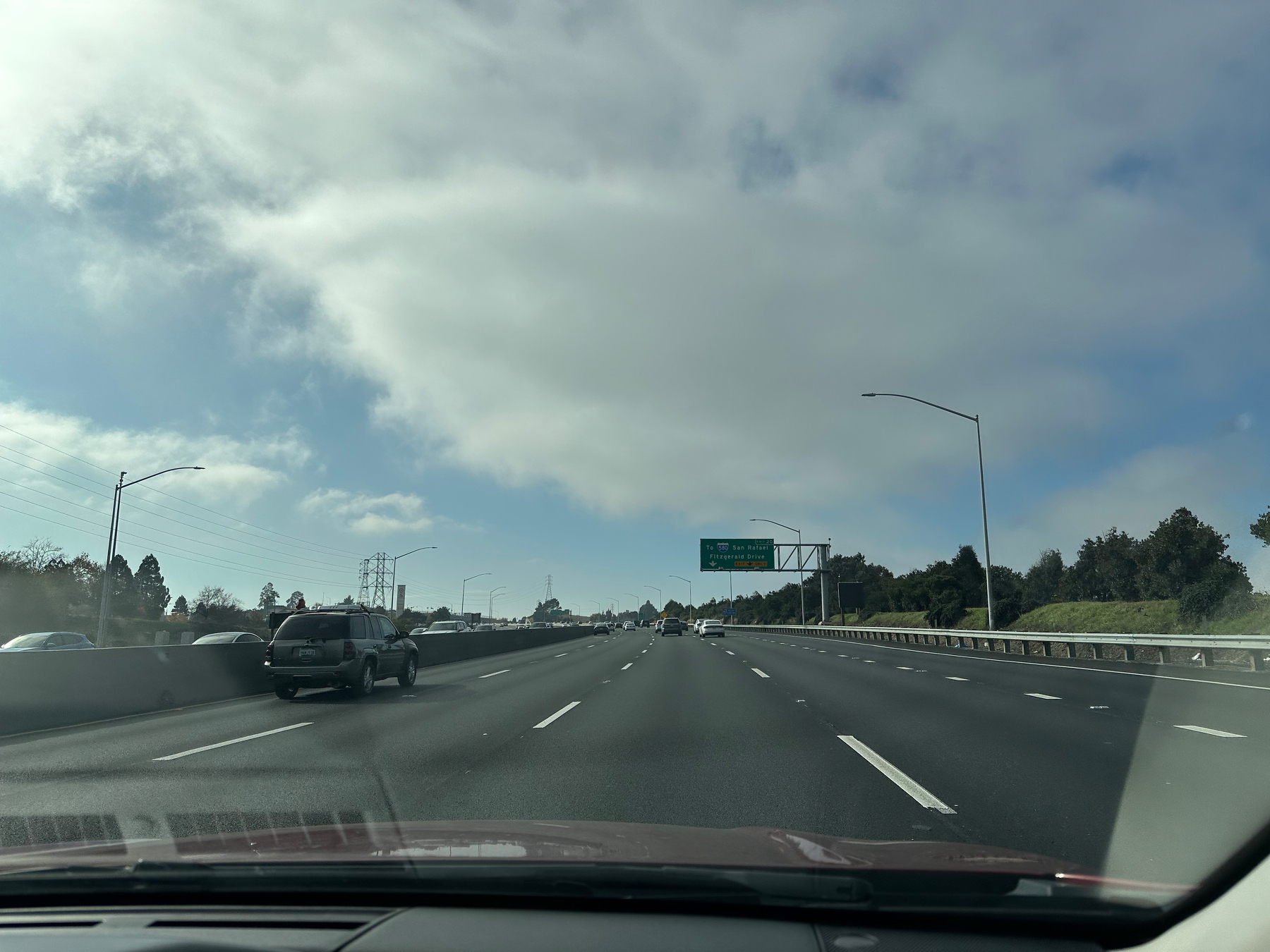 Photo in a moving car, passenger side, showing the end of a fog or low stratus clouds above a freeway. 
