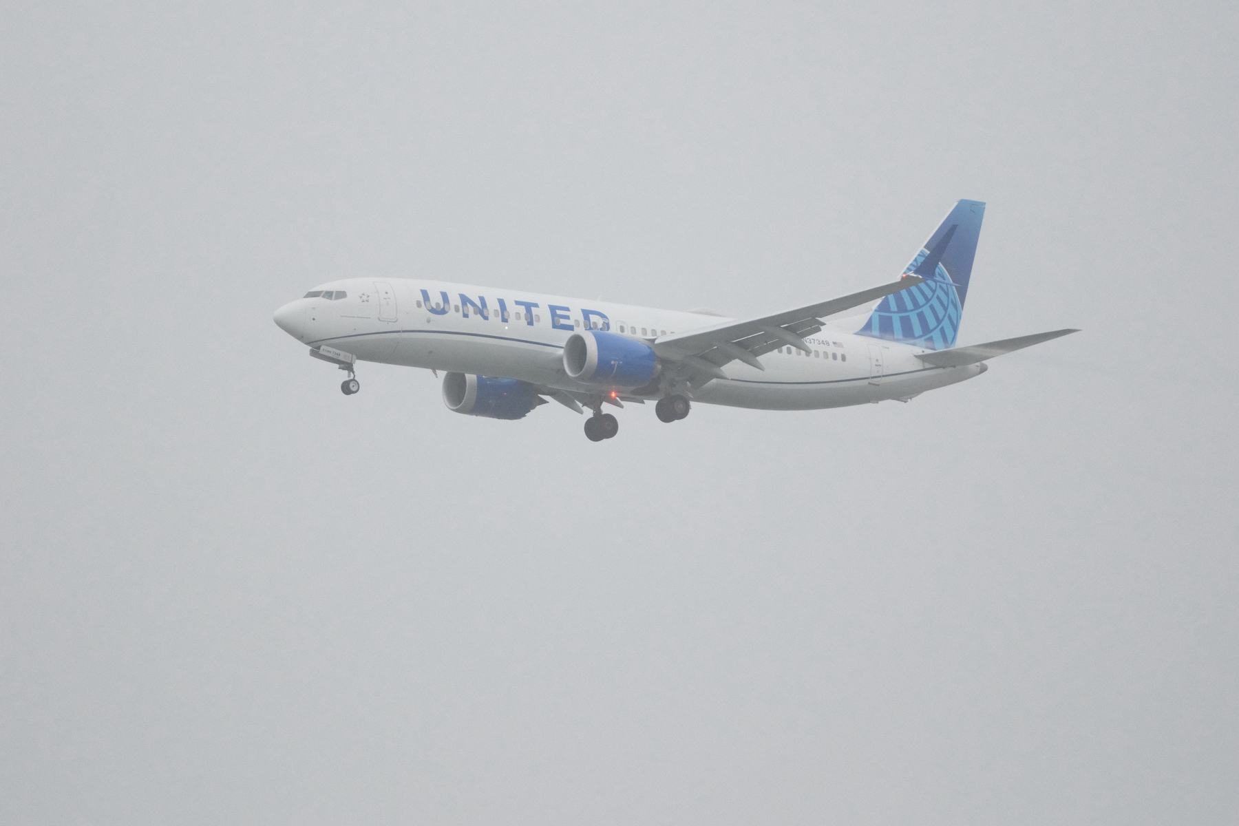 DSCF7540.JPG A Boeing 737 is on approach to SFO, with its gear down, under very overcast skies. Its red beacon lights are visible. Some moisture vortices can be seen streaming off its flaps and under its elevators.