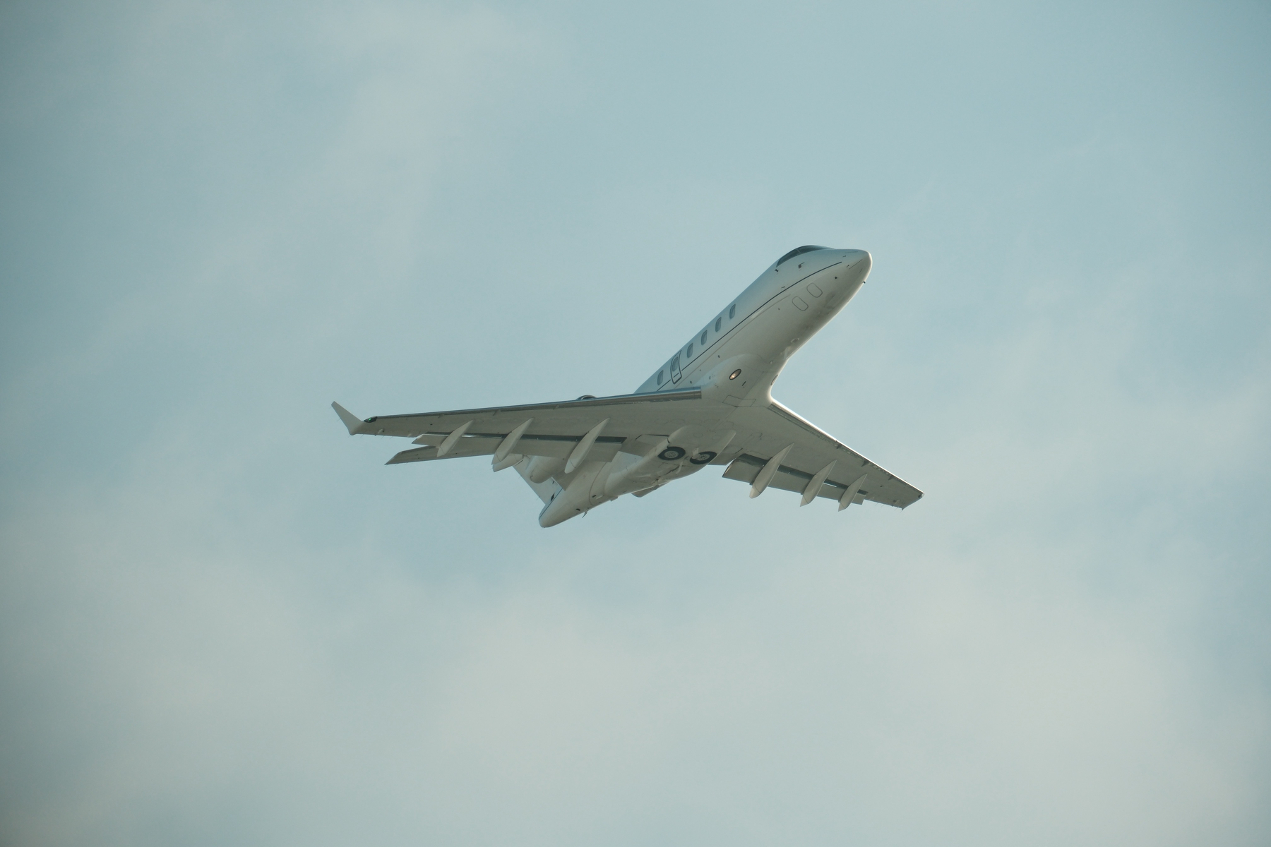 A private or business jet taking off from SFO 28R, showing its belly, with its gears up and a bit of wispy clouds behind it. Its flaps are still slightly down.