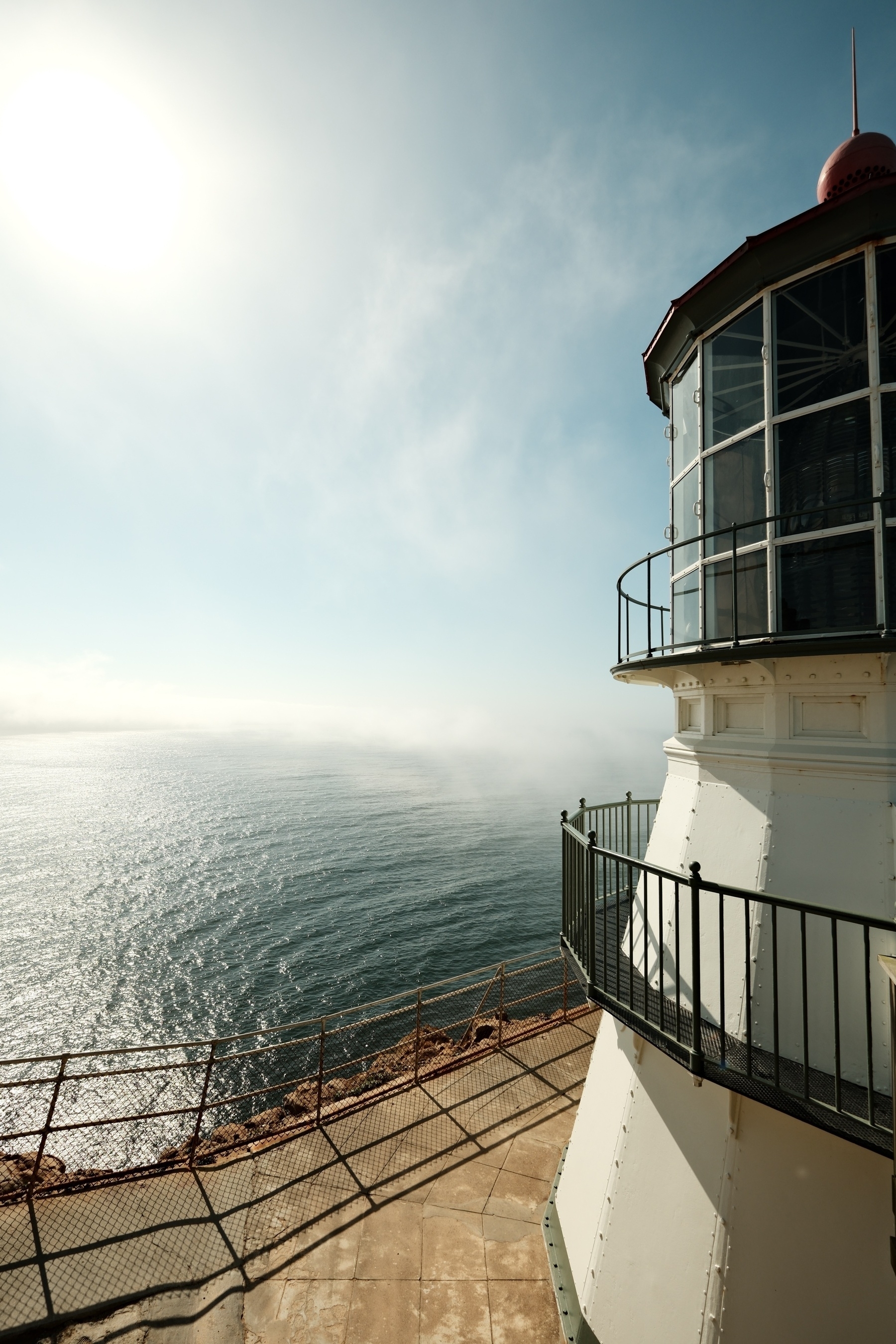 The lighthouse frames the right side of the photo, where the sky is slowly being revealed by passing low clouds or fog. The sea is calm.