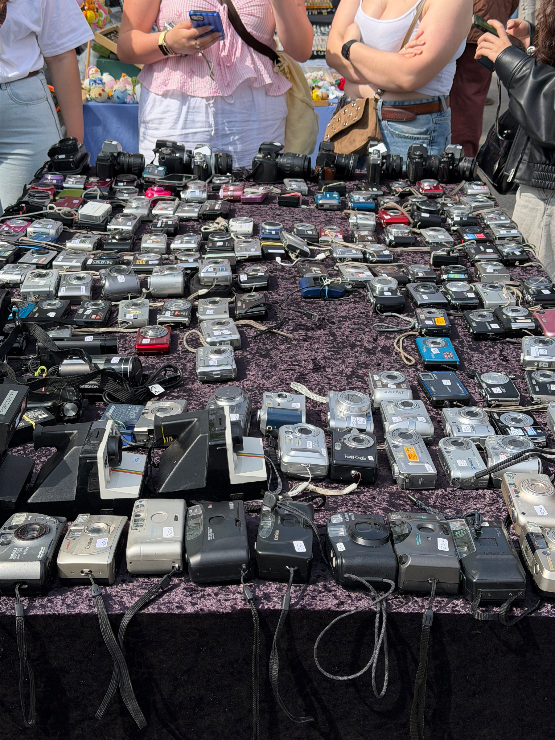 Rows of old school digital cameras on a table. These are 2000-2015ish vintage. 