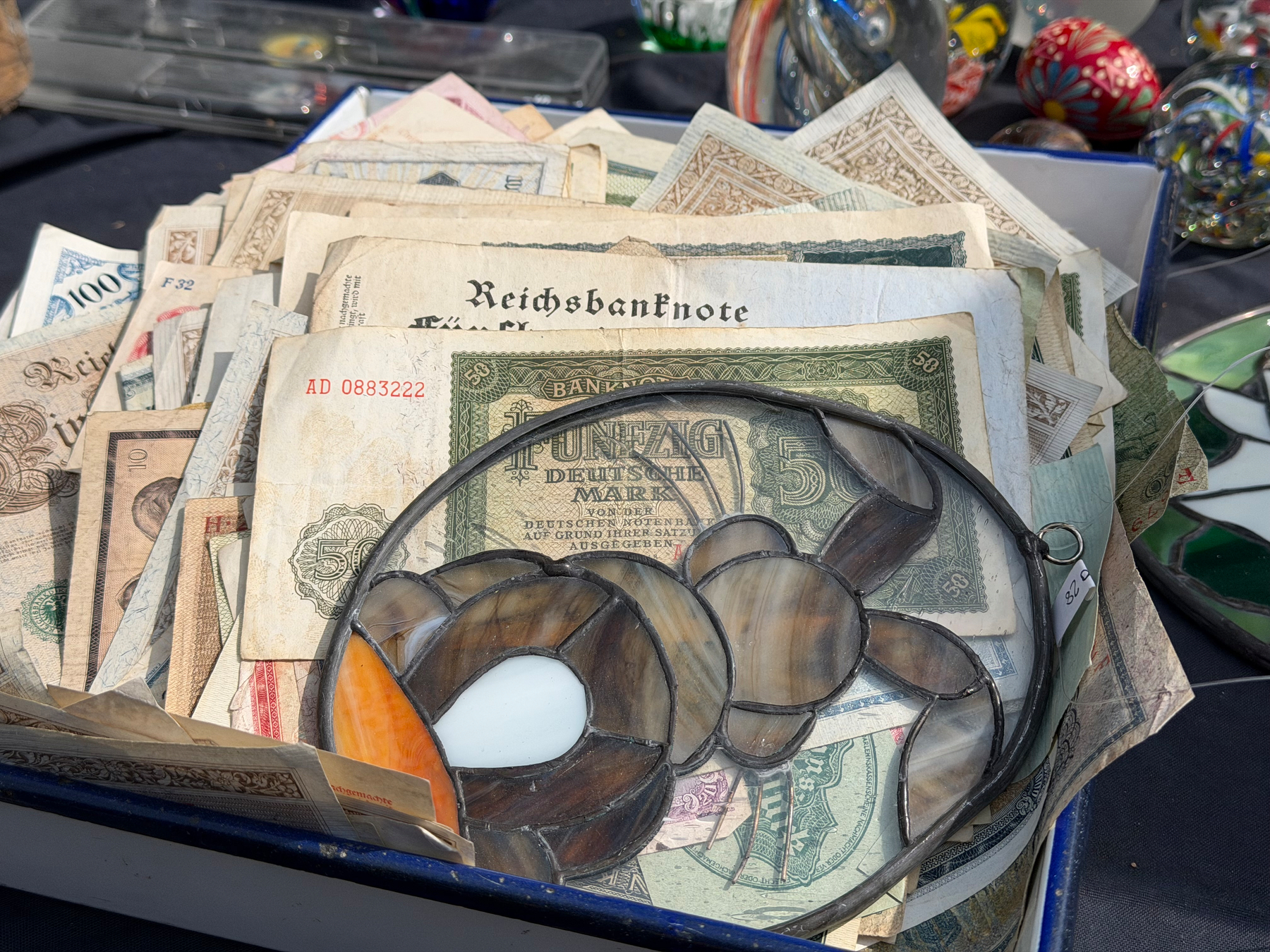 A mix of Deutsche Marks, Reichsmarks, Ostmarks with a flat stained glass bunny holding it all down 