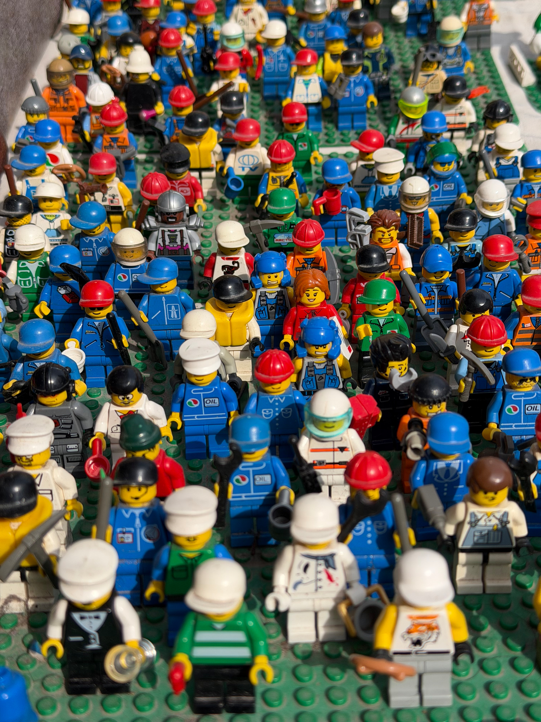 A crowd of LEGO people on a green Lego board. These are mostly wearing work uniforms.