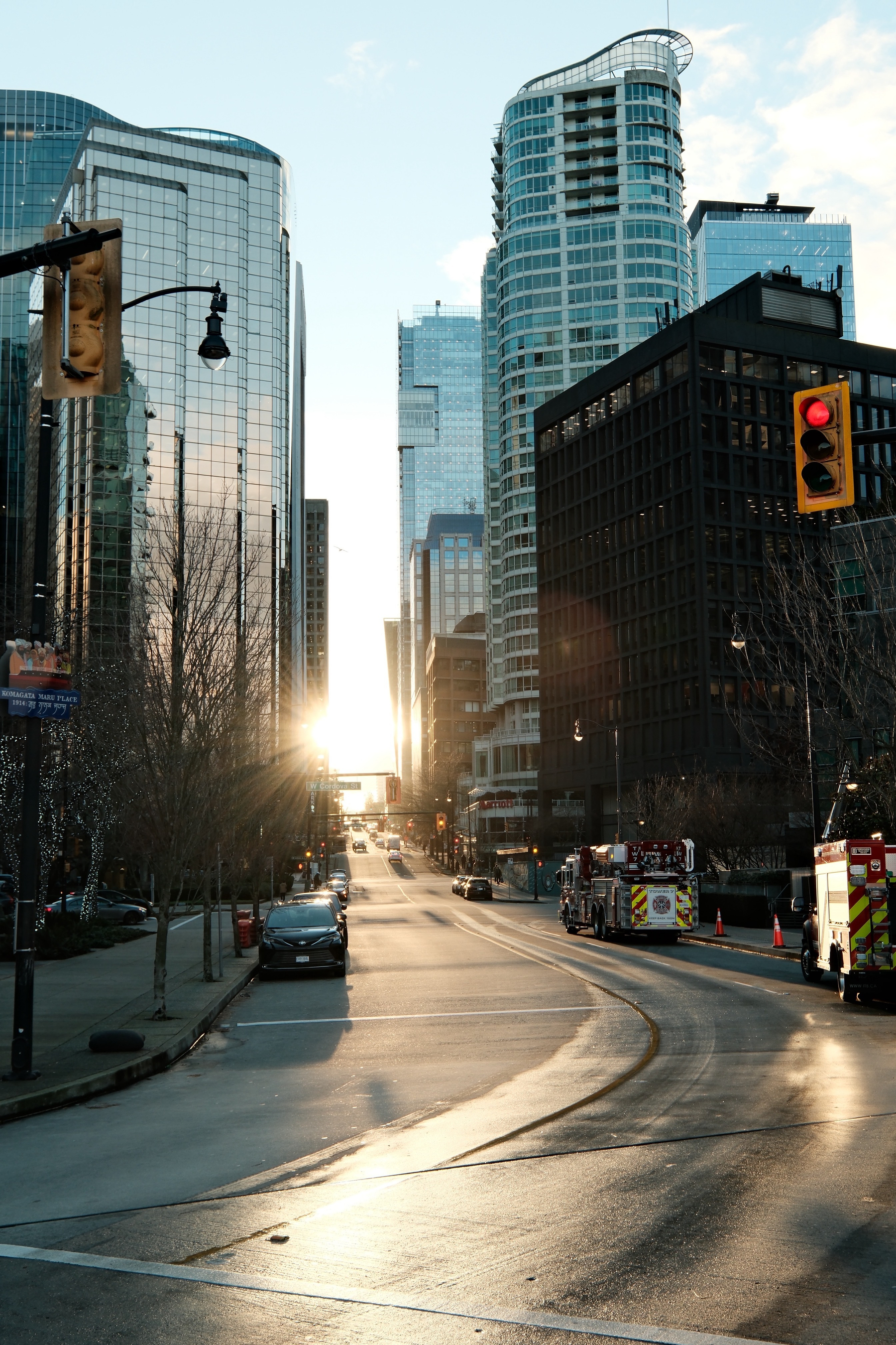 DSCF9271.jpg Thurlow Street is still damp from rain as the sun sets between tower buildings along Thurlow Street. Sunlight reflects off damp streets and there are two fire engines parked on the right-side of the road. A nearby traffic signal has a red light.